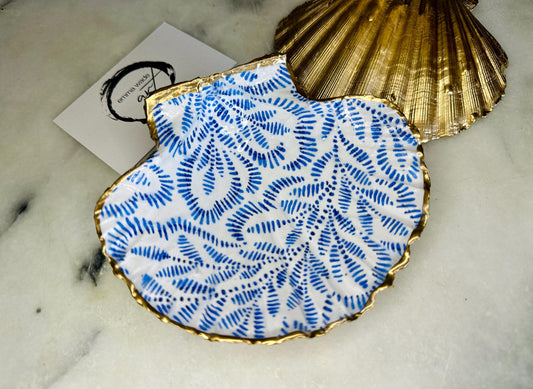 Handmade block print scallop shell trinket dish featuring a blue leaf pattern, finished with gilded gold leaf edges and sealed with a glossy resin. Crafted from a natural Dorset scallop shell, shown as a decorative jewellery tray on a light background, perfect for rings, earrings and small keepsakes. Coastal-inspired home decor, ideal for a bedside table, dressing table or bathroom, each piece one of a kind.
