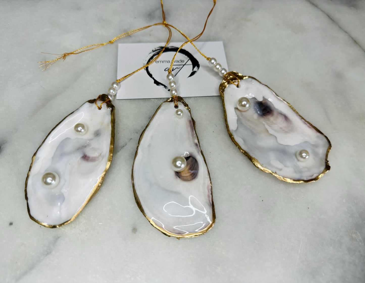 Luxury flat pearl oyster shell hanging ornaments handcrafted from natural Dorset oyster shells with glossy pearlescent interiors, two Swarovski pearls per ornament and hand-painted gold leaf edging. Elegant coastal hanging decor finished in crystal clear resin with gold hanging cord and pearl bead details. Available individually or as a set of three. Perfect for beach house interiors, luxury bathroom styling, wedding gifts, coastal Christmas decor and year-round shell home decor.
