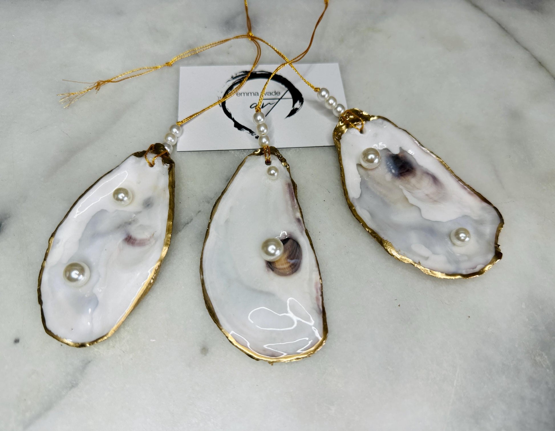 Luxury flat pearl oyster shell hanging ornaments handcrafted from natural Dorset oyster shells with glossy pearlescent interiors, two Swarovski pearls per ornament and hand-painted gold leaf edging. Elegant coastal hanging decor finished in crystal clear resin with gold hanging cord and pearl bead details. Available individually or as a set of three. Perfect for beach house interiors, luxury bathroom styling, wedding gifts, coastal Christmas decor and year-round shell home decor.