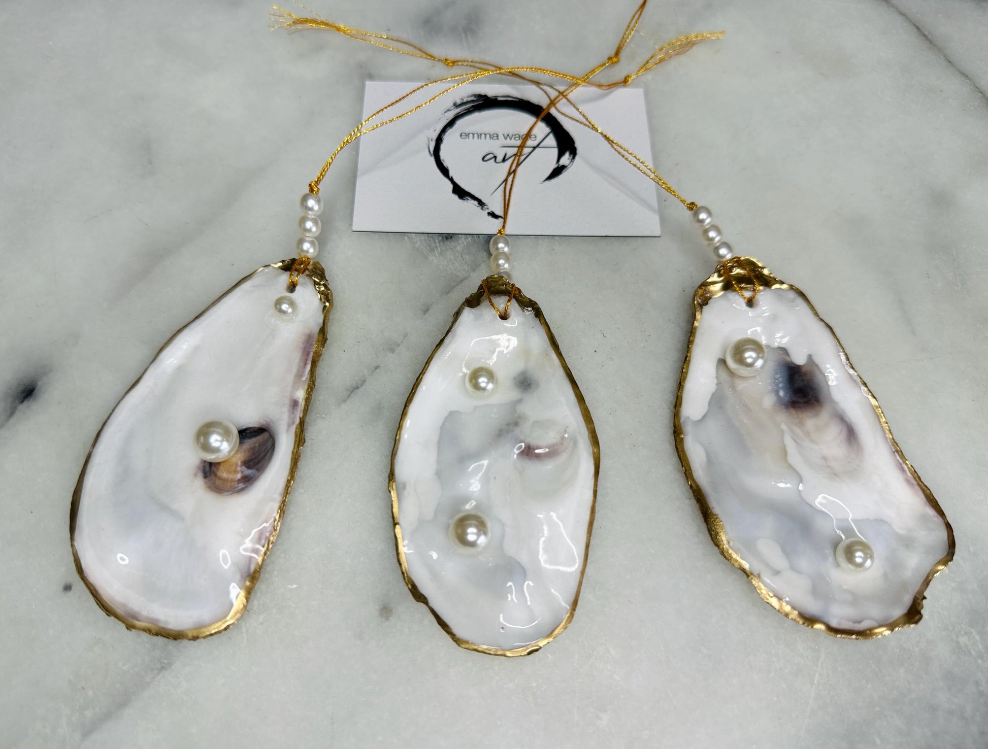 Luxury flat pearl oyster shell hanging ornaments handcrafted from natural Dorset oyster shells with glossy pearlescent interiors, two Swarovski pearls per ornament and hand-painted gold leaf edging. Elegant coastal hanging decor finished in crystal clear resin with gold hanging cord and pearl bead details. Available individually or as a set of three. Perfect for beach house interiors, luxury bathroom styling, wedding gifts, coastal Christmas decor and year-round shell home decor.