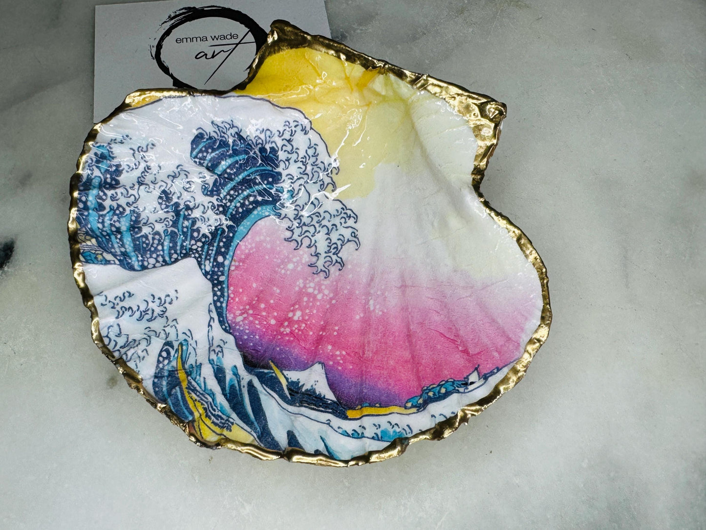 Handcrafted Great Wave of Kanagawa scallop shell trinket dish inspired by Hokusai’s iconic Japanese woodblock print. Each Dorset shell is hand-drawn, painted, and sealed in resin, with a choice of Dawn or Dusk design. Finished with a natural varnished back and gold rim or fully gilded in liquid gold leaf. A unique handmade jewellery holder or coastal art gift, beautifully presented in sustainable packaging.