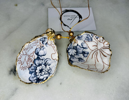 Handmade blue floral oyster shell hanging ornament shown as a single piece, decoupaged with a Palmer’s print style floral design, hand-gilded with gold leaf and sealed with glossy resin. Crafted from a natural Dorset oyster shell and finished with a gold hanging string. Coastal-inspired decorative ornament, perfect for Christmas trees, botanical home decor or a unique handmade gift. Each shell is one of a kind.