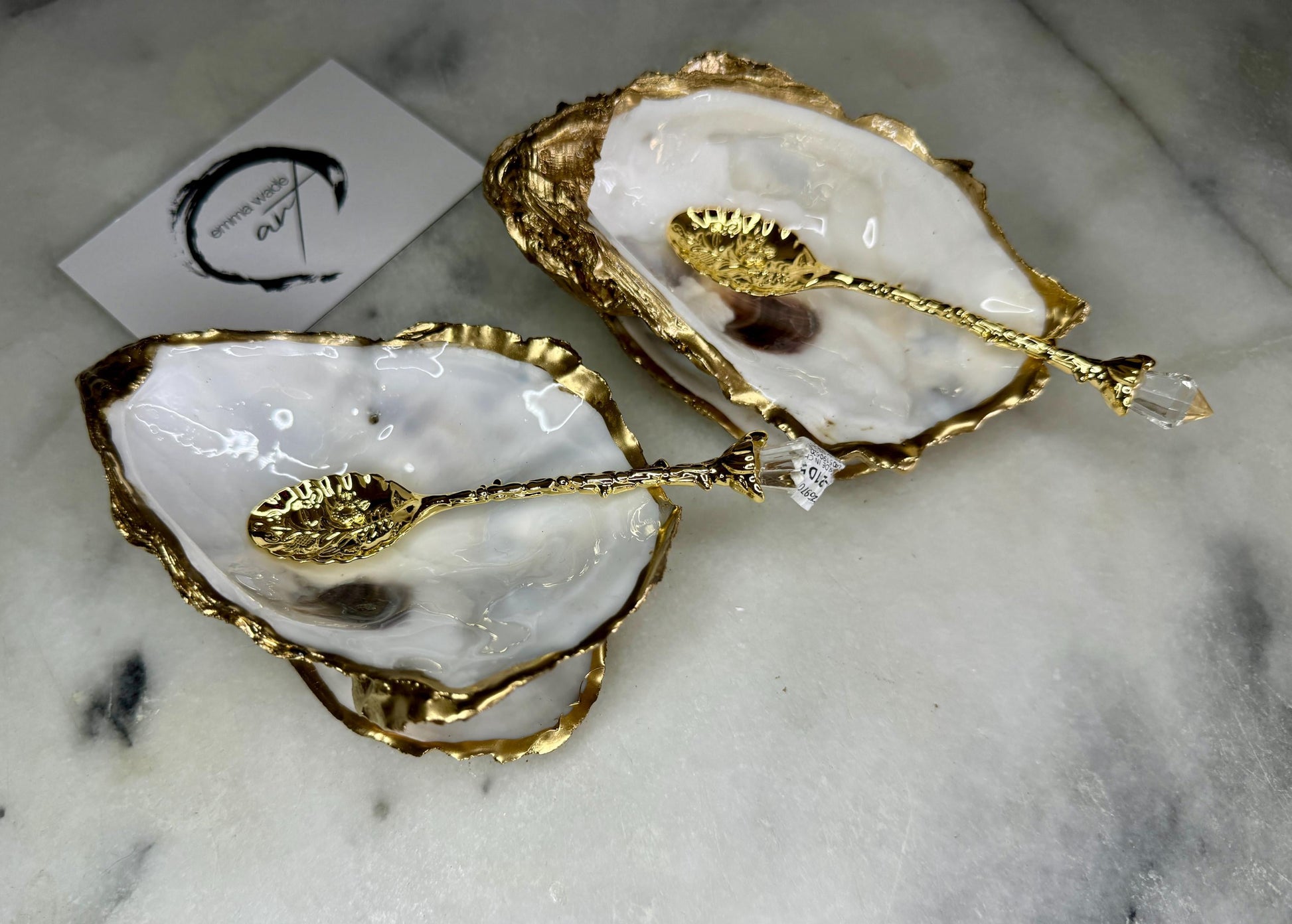 Handmade gold leaf oyster shell salt cellar set with pearl interiors and matching spoons. Coastal pinch pots made from Dorset oyster shells, sealed with glossy resin and finished with gilded edges. Luxury tableware set photographed on a light background, showing two shell salt dishes and decorative spoons, perfect for serving salt or spices at the table.