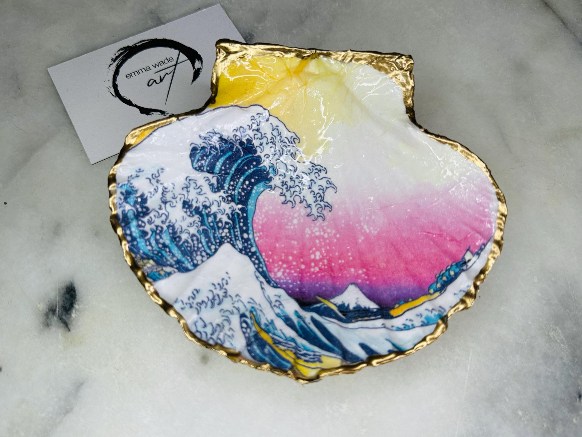 Handcrafted Great Wave of Kanagawa scallop shell trinket dish inspired by Hokusai’s iconic Japanese woodblock print. Each Dorset shell is hand-drawn, painted, and sealed in resin, with a choice of Dawn or Dusk design. Finished with a natural varnished back and gold rim or fully gilded in liquid gold leaf. A unique handmade jewellery holder or coastal art gift, beautifully presented in sustainable packaging.