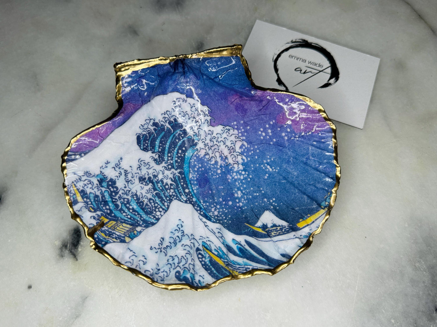 Handcrafted Great Wave of Kanagawa scallop shell trinket dish inspired by Hokusai’s iconic Japanese woodblock print. Each Dorset shell is hand-drawn, painted, and sealed in resin, with a choice of Dawn or Dusk design. Finished with a natural varnished back and gold rim or fully gilded in liquid gold leaf. A unique handmade jewellery holder or coastal art gift, beautifully presented in sustainable packaging.