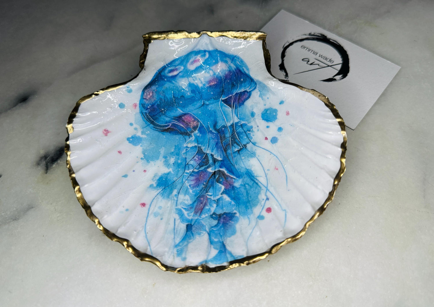 Hand illustrated blue jellyfish scallop shell trinket dish featuring original Emma Wade ART watercolour artwork. Natural Dorset scallop shell finished with hand-gilded gold leaf edging and crystal-clear resin gloss. Coastal jewellery dish, ring holder, trinket tray and ocean-inspired home decor gift. Blue and pink jellyfish design with luxury gold finish, handmade in Surrey, UK.