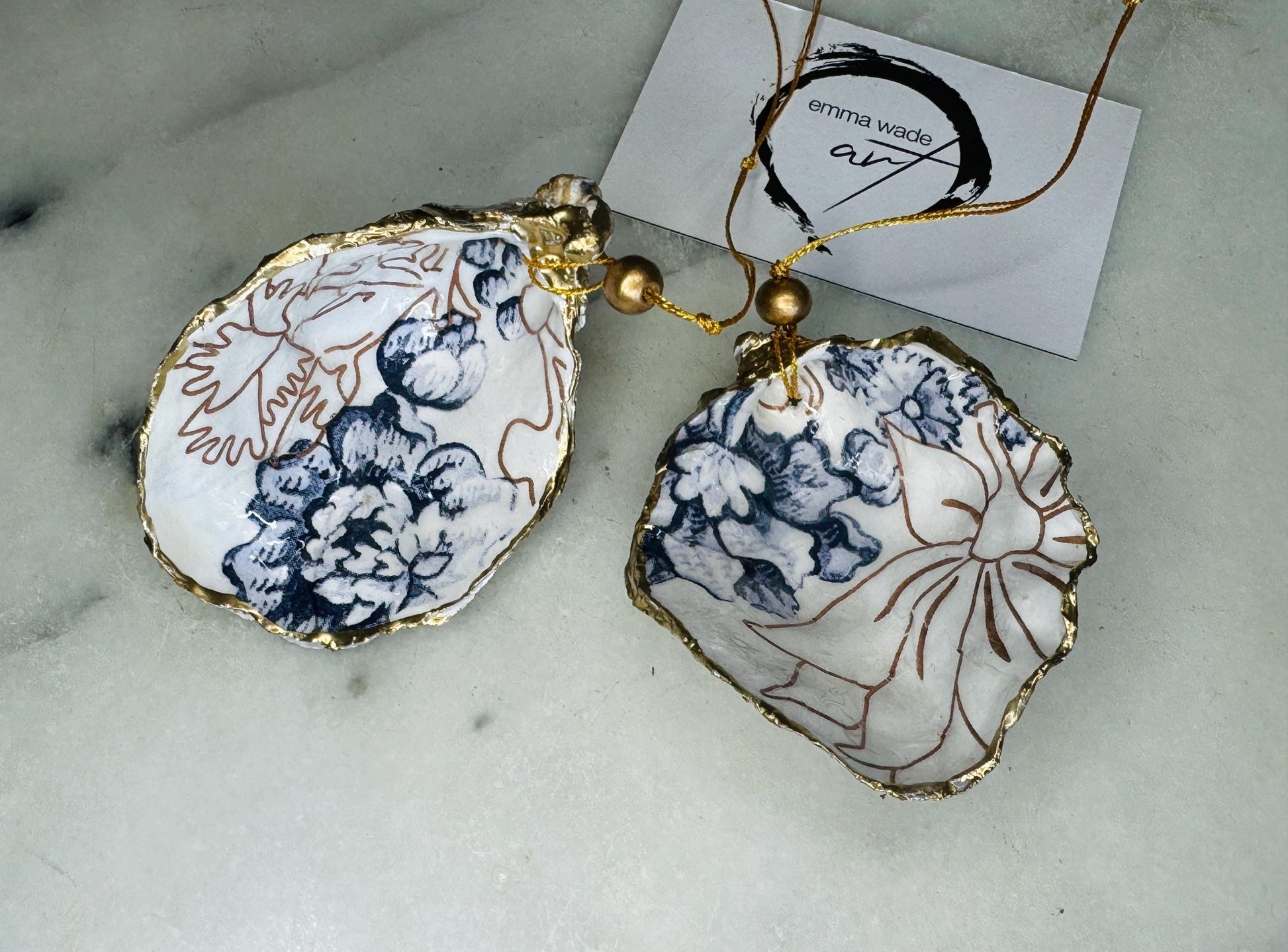 Handmade blue floral oyster shell hanging ornament shown as a single piece, decoupaged with a Palmer’s print style floral design, hand-gilded with gold leaf and sealed with glossy resin. Crafted from a natural Dorset oyster shell and finished with a gold hanging string. Coastal-inspired decorative ornament, perfect for Christmas trees, botanical home decor or a unique handmade gift. Each shell is one of a kind.