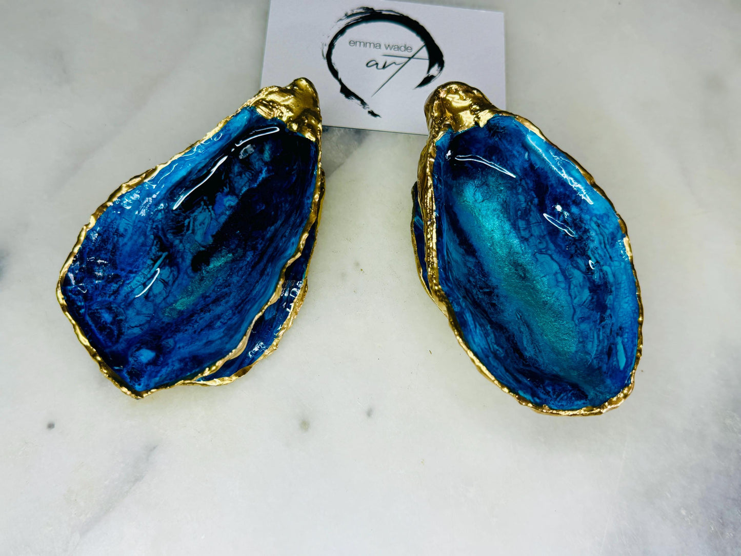 Blue oyster shell ring box, hand painted to resemble ocean waves in rich blue tones with metallic detail and finished with gold leaf edges. Includes a matching painted lid. Each shell is approx. 10cm and crafted from Dorset coastlines, making every piece unique. A stunning ocean-inspired jewellery box, ring bearer box, or proposal ring holder. Perfect for weddings, engagements, anniversaries, or as a keepsake gift for someone special who loves the sea.