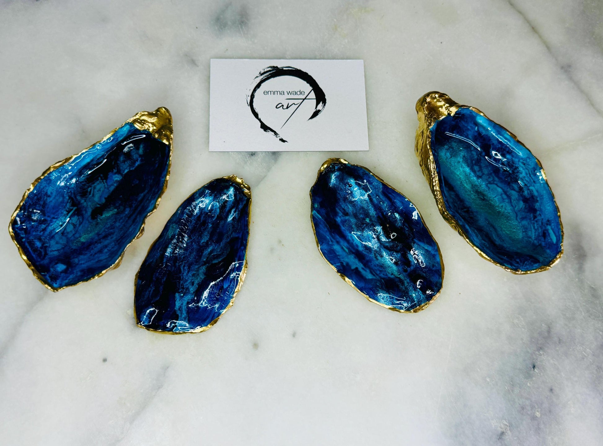 Blue oyster shell ring box, hand painted to resemble ocean waves in rich blue tones with metallic detail and finished with gold leaf edges. Includes a matching painted lid. Each shell is approx. 10cm and crafted from Dorset coastlines, making every piece unique. A stunning ocean-inspired jewellery box, ring bearer box, or proposal ring holder. Perfect for weddings, engagements, anniversaries, or as a keepsake gift for someone special who loves the sea.