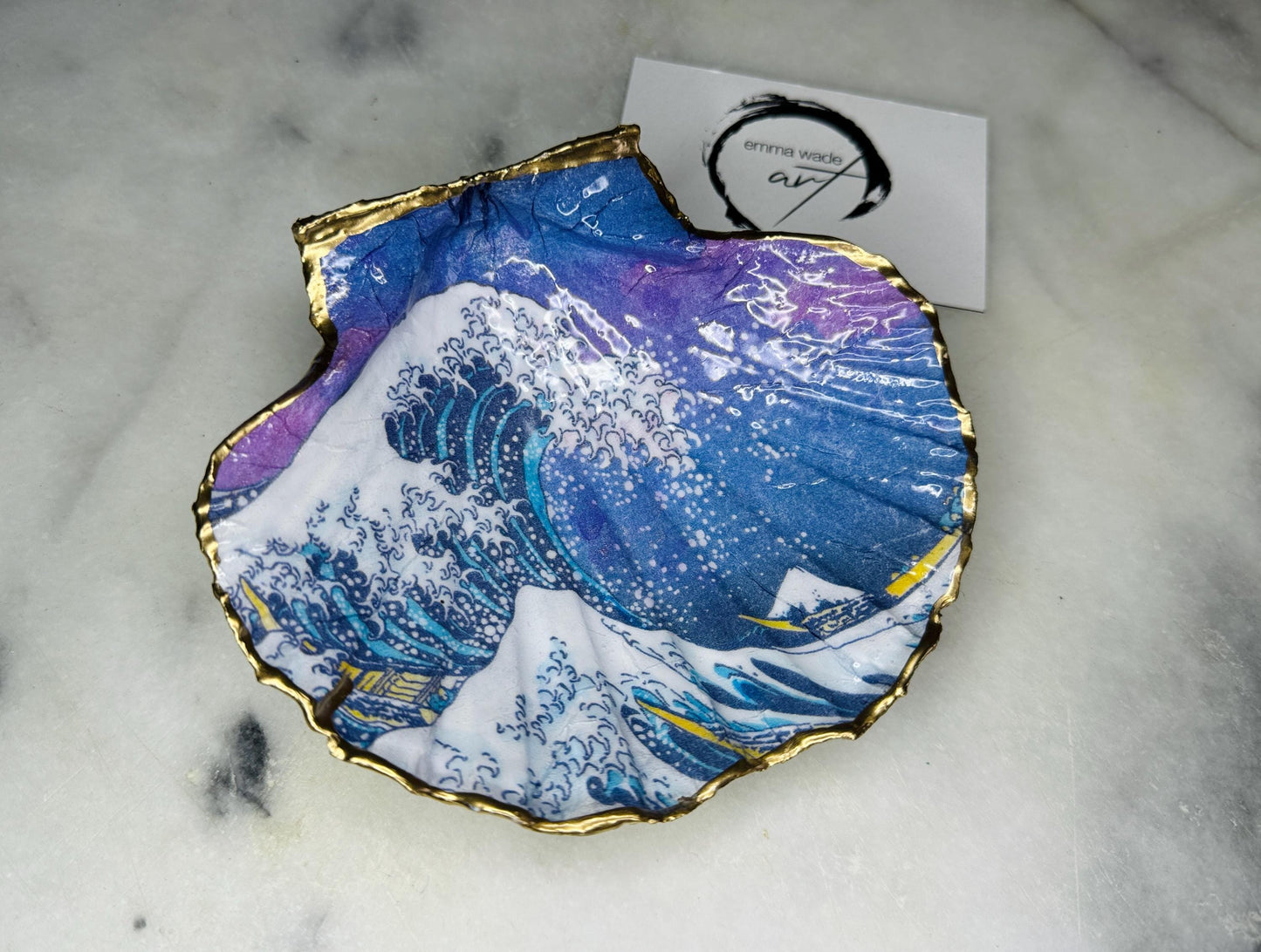 Handcrafted Great Wave of Kanagawa scallop shell trinket dish inspired by Hokusai’s iconic Japanese woodblock print. Each Dorset shell is hand-drawn, painted, and sealed in resin, with a choice of Dawn or Dusk design. Finished with a natural varnished back and gold rim or fully gilded in liquid gold leaf. A unique handmade jewellery holder or coastal art gift, beautifully presented in sustainable packaging.