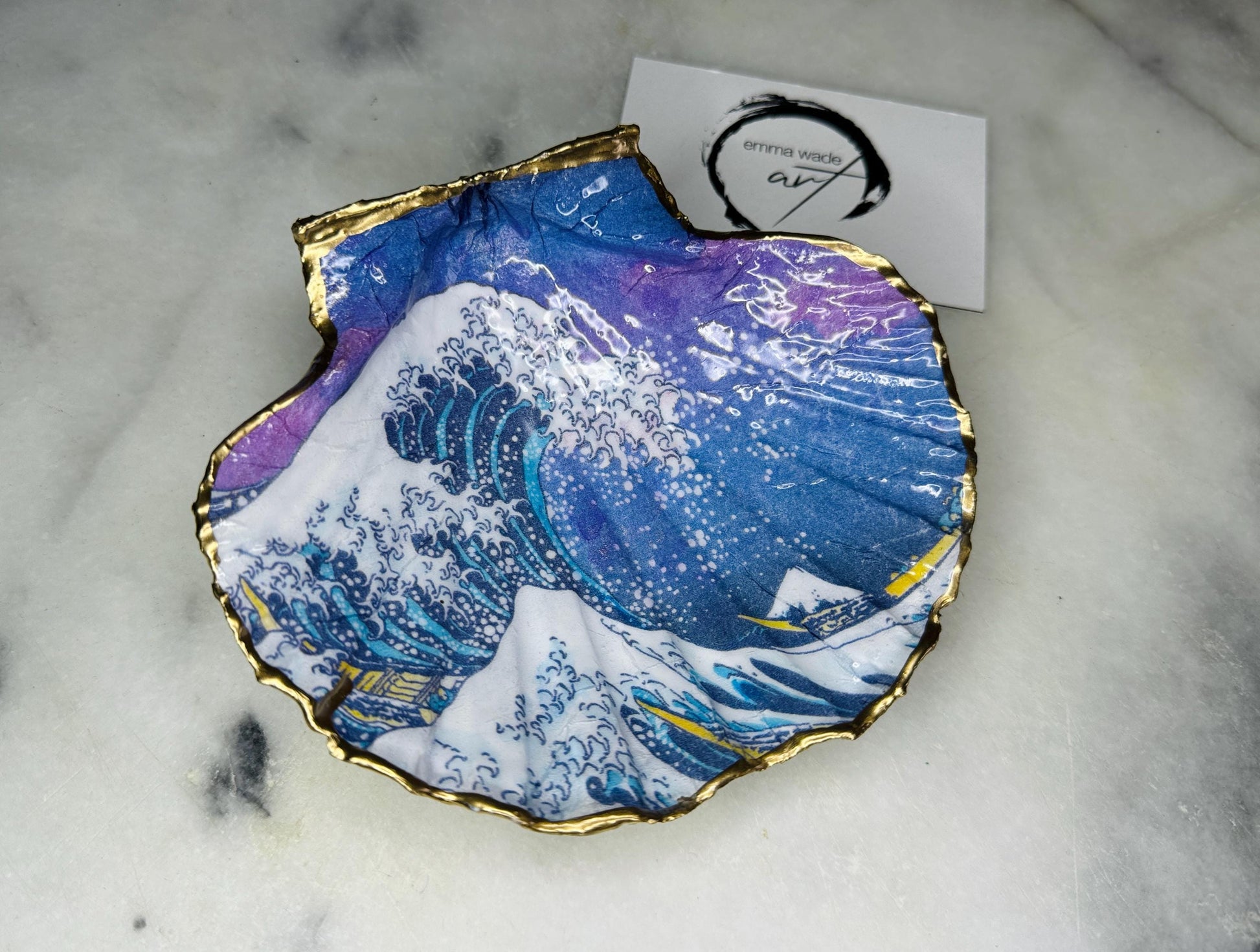 Handcrafted Great Wave of Kanagawa scallop shell trinket dish inspired by Hokusai’s iconic Japanese woodblock print. Each Dorset shell is hand-drawn, painted, and sealed in resin, with a choice of Dawn or Dusk design. Finished with a natural varnished back and gold rim or fully gilded in liquid gold leaf. A unique handmade jewellery holder or coastal art gift, beautifully presented in sustainable packaging.