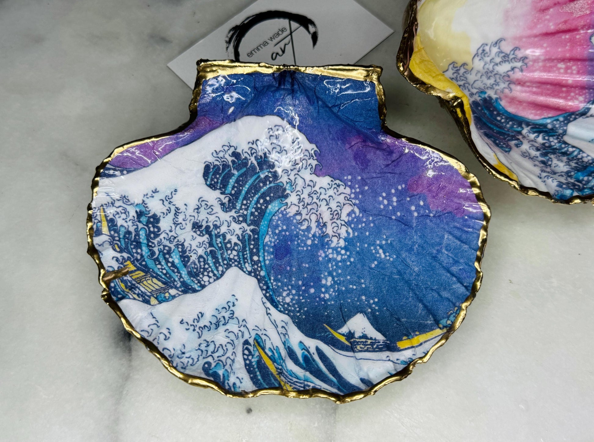 Handcrafted Great Wave of Kanagawa scallop shell trinket dish inspired by Hokusai’s iconic Japanese woodblock print. Each Dorset shell is hand-drawn, painted, and sealed in resin, with a choice of Dawn or Dusk design. Finished with a natural varnished back and gold rim or fully gilded in liquid gold leaf. A unique handmade jewellery holder or coastal art gift, beautifully presented in sustainable packaging.