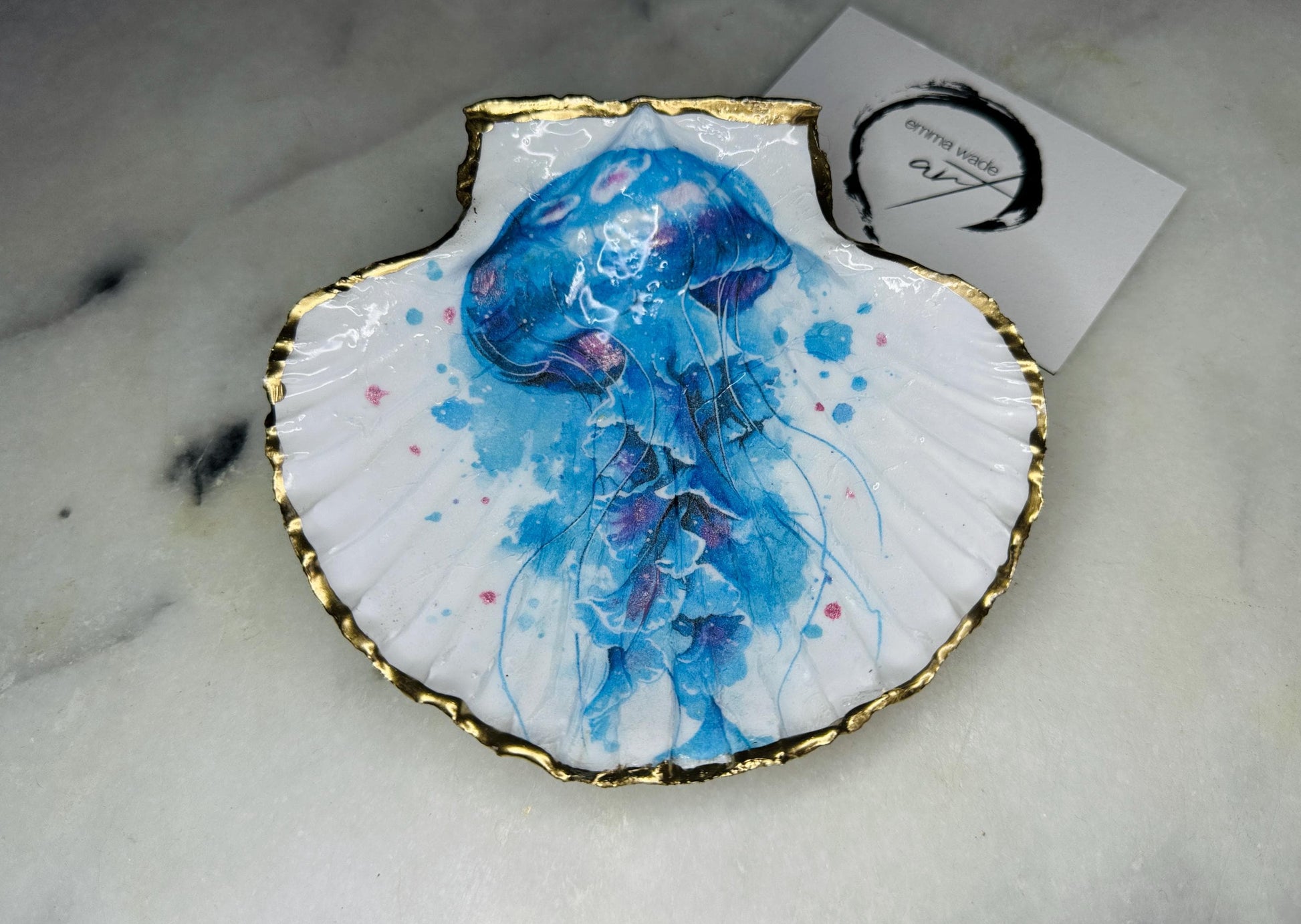 Hand illustrated blue jellyfish scallop shell trinket dish featuring original Emma Wade ART watercolour artwork. Natural Dorset scallop shell finished with hand-gilded gold leaf edging and crystal-clear resin gloss. Coastal jewellery dish, ring holder, trinket tray and ocean-inspired home decor gift. Blue and pink jellyfish design with luxury gold finish, handmade in Surrey, UK.
