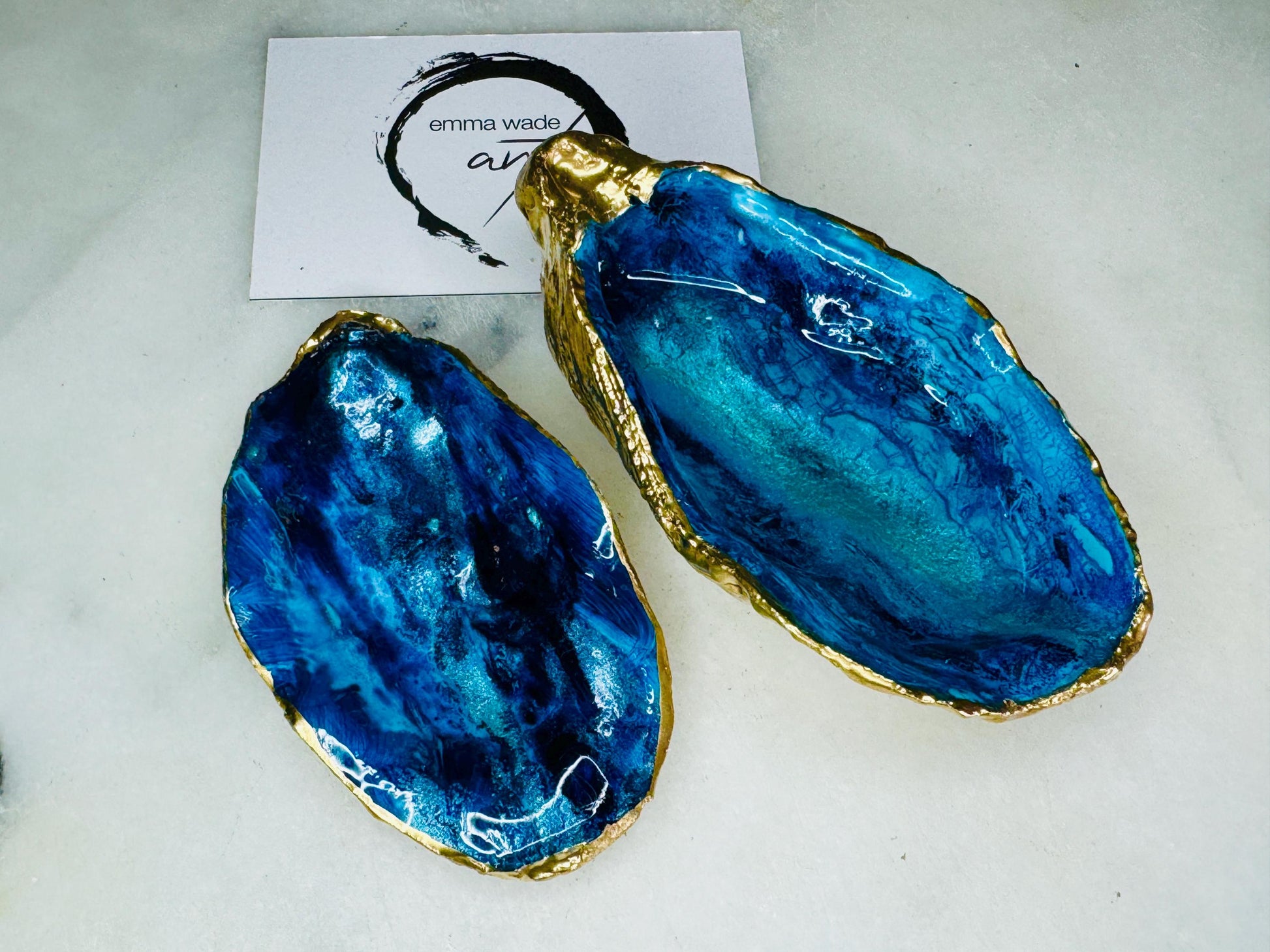 Blue oyster shell ring box, hand painted to resemble ocean waves in rich blue tones with metallic detail and finished with gold leaf edges. Includes a matching painted lid. Each shell is approx. 10cm and crafted from Dorset coastlines, making every piece unique. A stunning ocean-inspired jewellery box, ring bearer box, or proposal ring holder. Perfect for weddings, engagements, anniversaries, or as a keepsake gift for someone special who loves the sea.