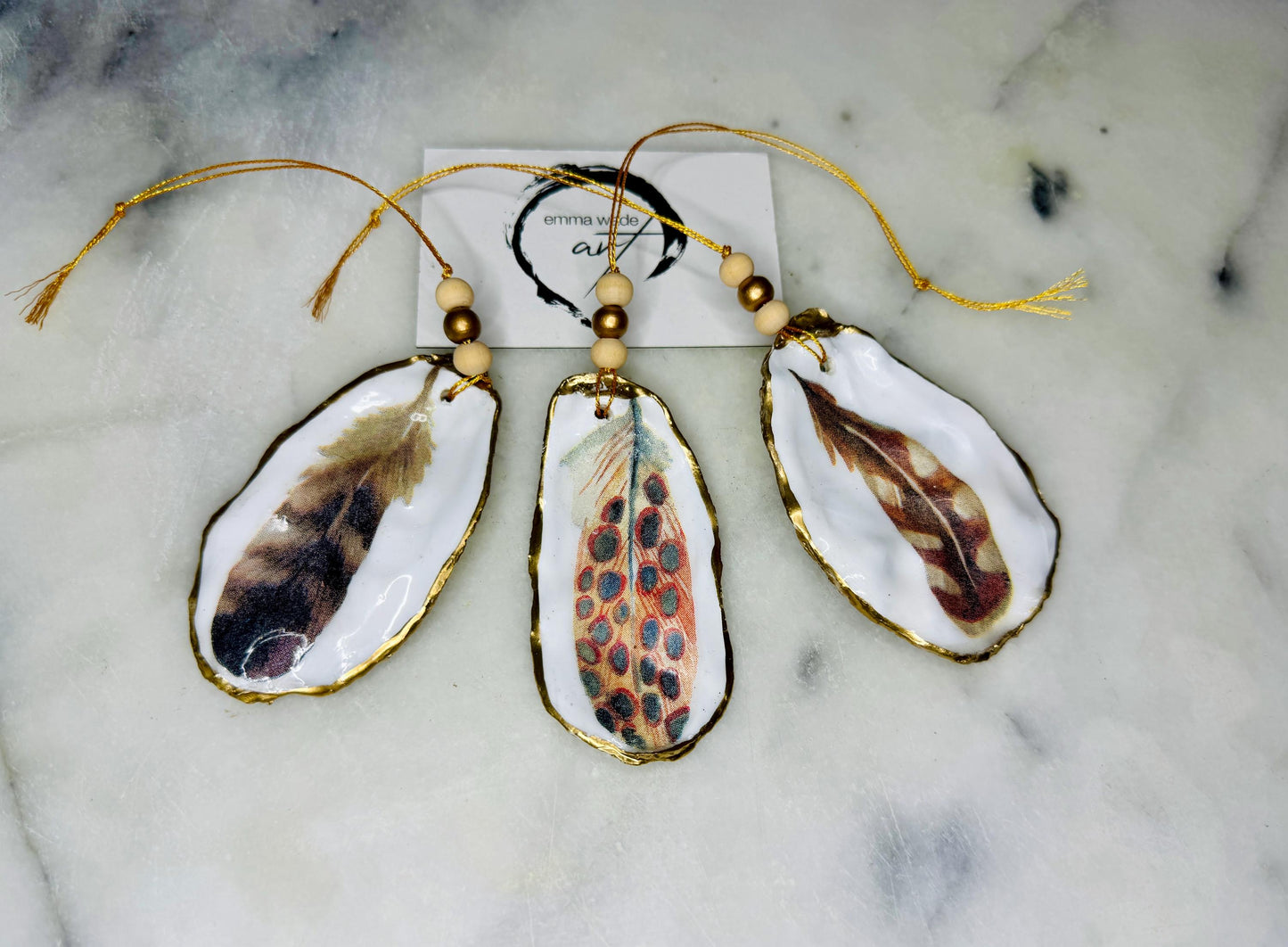Aquarelle feather oyster shell hanging ornaments, handmade coastal décor, gilded gold leaf shells, resin sealed feather decorations, Christmas tree ornaments, nature-inspired gifts, watercolor feather oyster shells, Dorset handmade shell ornaments, sustainable coastal gifts, oyster shell art, feather design decorations, unique shell ornaments, eco-friendly handmade oyster shell Christmas gifts.