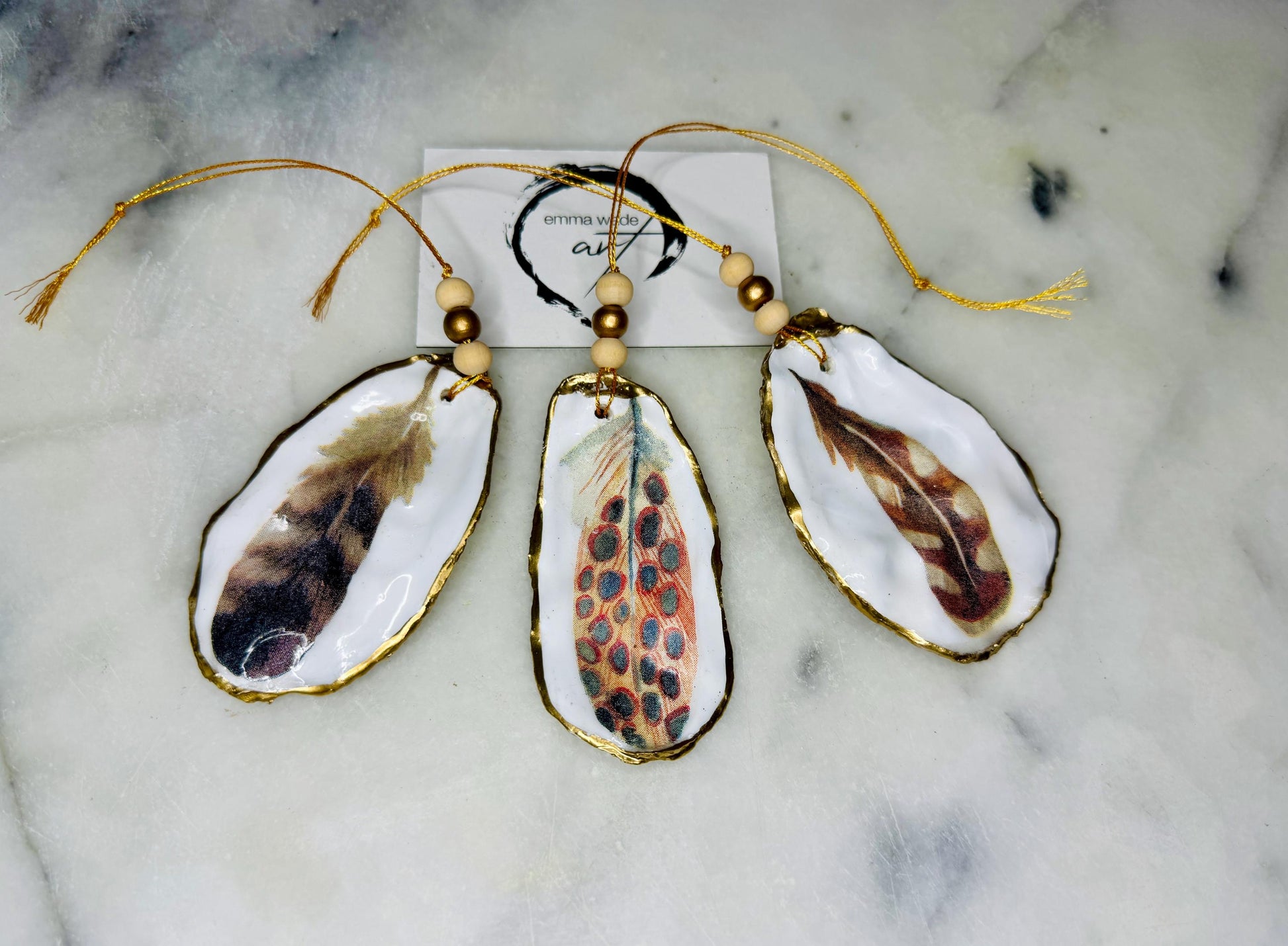 Aquarelle feather oyster shell hanging ornaments, handmade coastal décor, gilded gold leaf shells, resin sealed feather decorations, Christmas tree ornaments, nature-inspired gifts, watercolor feather oyster shells, Dorset handmade shell ornaments, sustainable coastal gifts, oyster shell art, feather design decorations, unique shell ornaments, eco-friendly handmade oyster shell Christmas gifts.