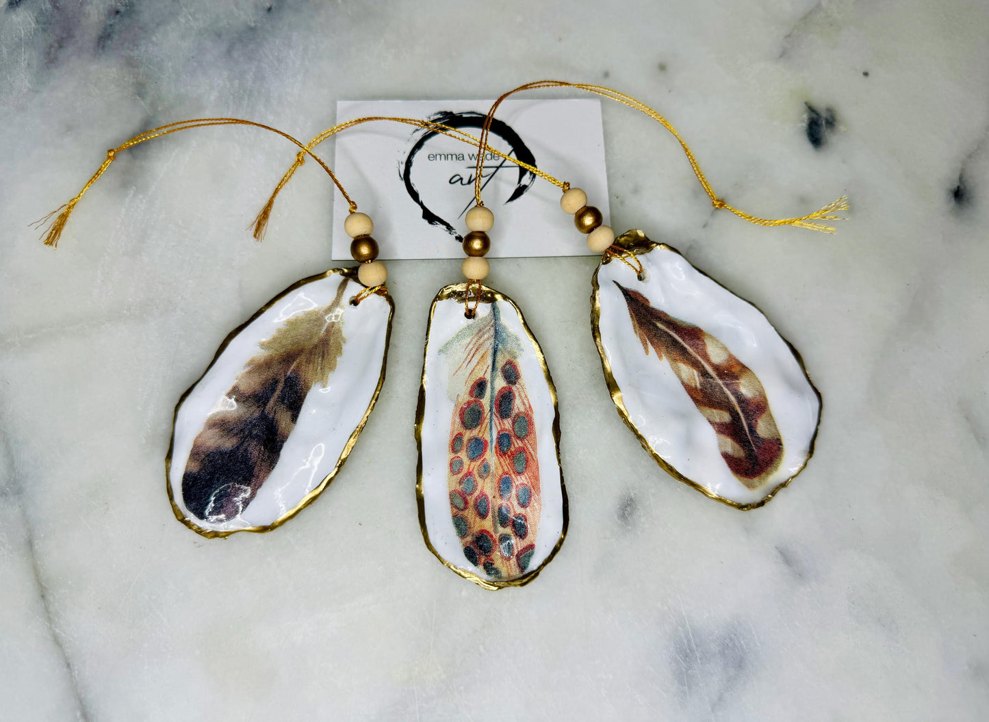 Aquarelle feather oyster shell hanging ornaments, handmade coastal décor, gilded gold leaf shells, resin sealed feather decorations, Christmas tree ornaments, nature-inspired gifts, watercolor feather oyster shells, Dorset handmade shell ornaments, sustainable coastal gifts, oyster shell art, feather design decorations, unique shell ornaments, eco-friendly handmade oyster shell Christmas gifts.