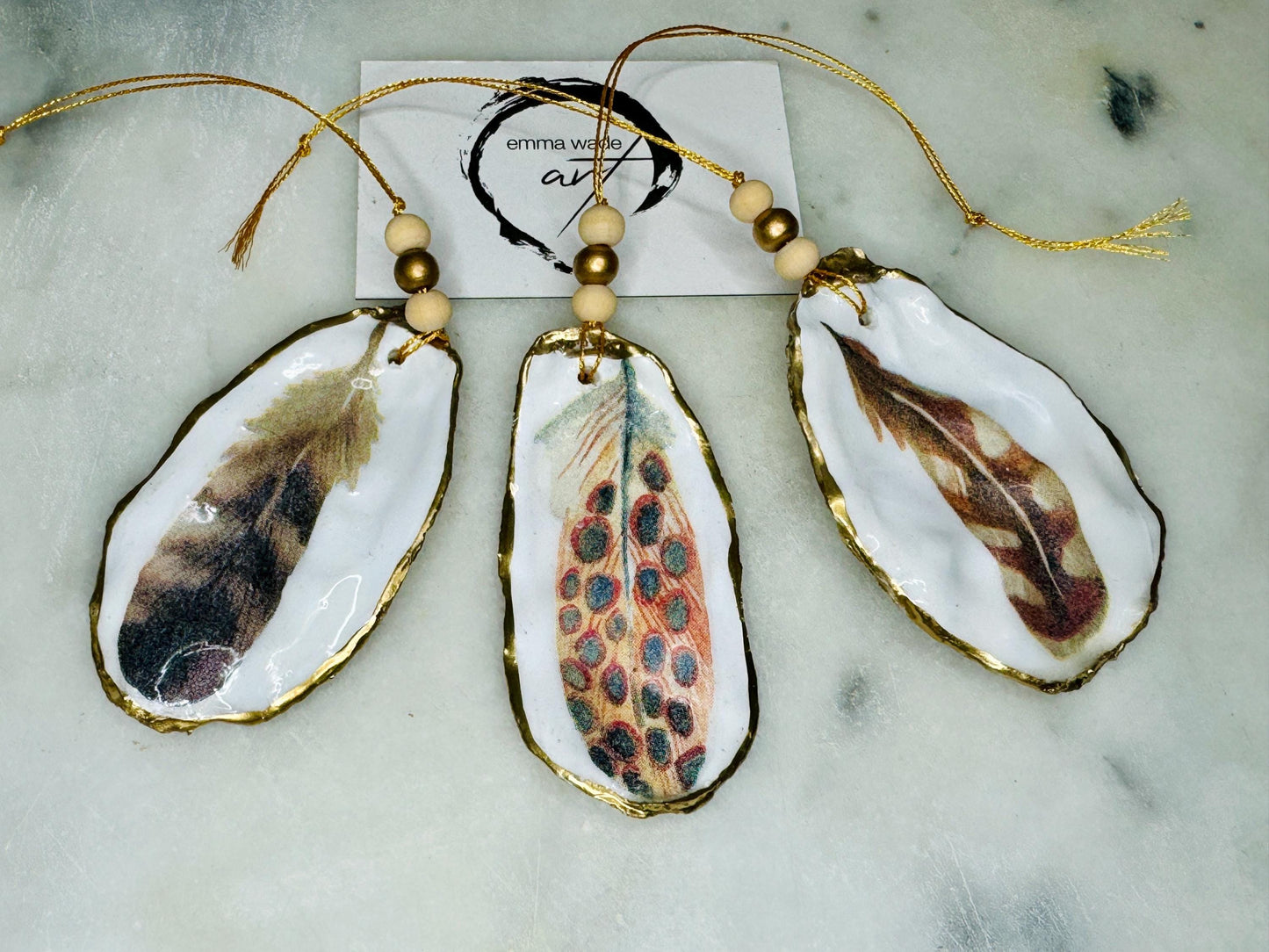 Aquarelle feather oyster shell hanging ornaments, handmade coastal décor, gilded gold leaf shells, resin sealed feather decorations, Christmas tree ornaments, nature-inspired gifts, watercolor feather oyster shells, Dorset handmade shell ornaments, sustainable coastal gifts, oyster shell art, feather design decorations, unique shell ornaments, eco-friendly handmade oyster shell Christmas gifts.