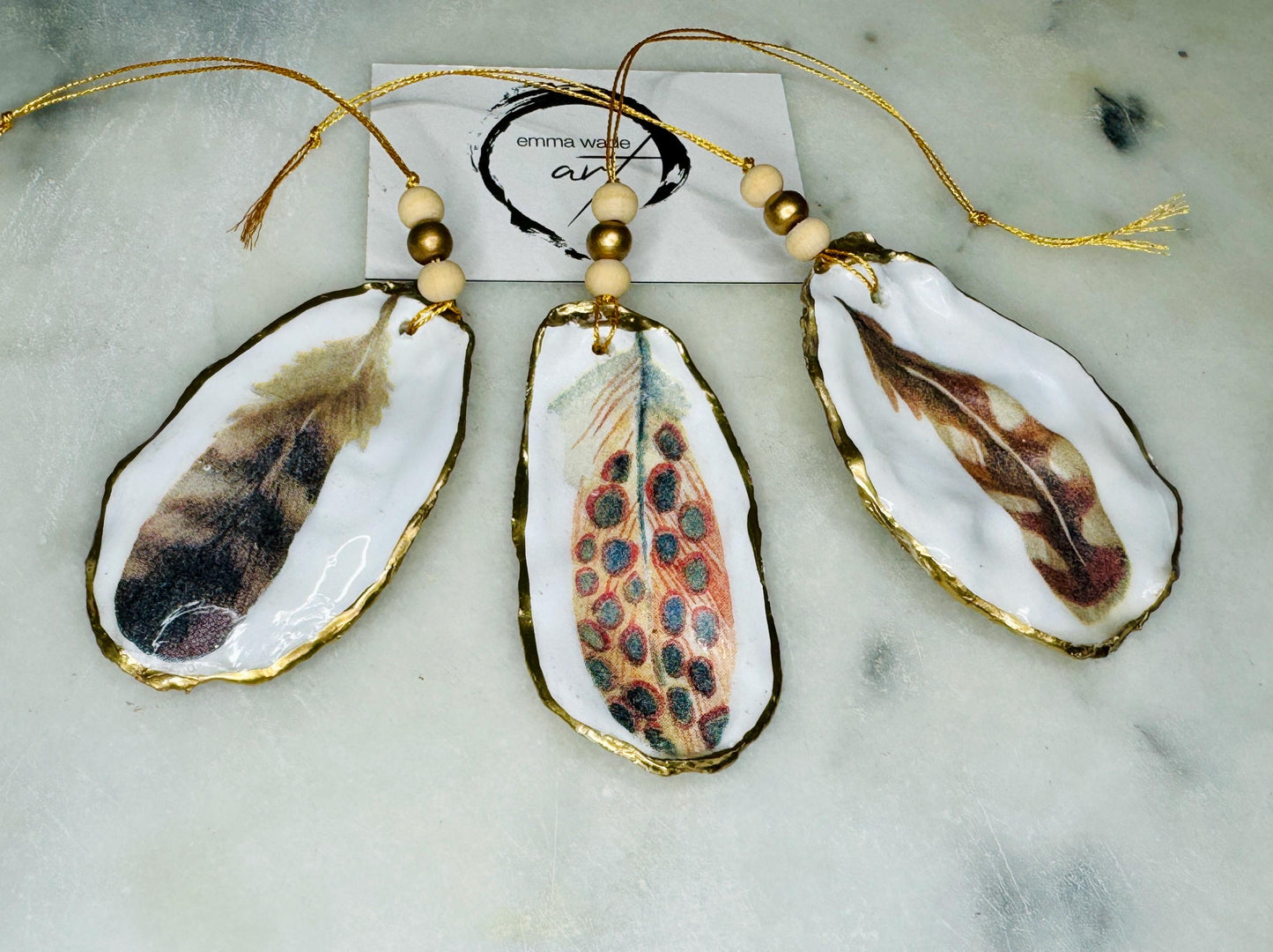Aquarelle feather oyster shell hanging ornaments, handmade coastal décor, gilded gold leaf shells, resin sealed feather decorations, Christmas tree ornaments, nature-inspired gifts, watercolor feather oyster shells, Dorset handmade shell ornaments, sustainable coastal gifts, oyster shell art, feather design decorations, unique shell ornaments, eco-friendly handmade oyster shell Christmas gifts.