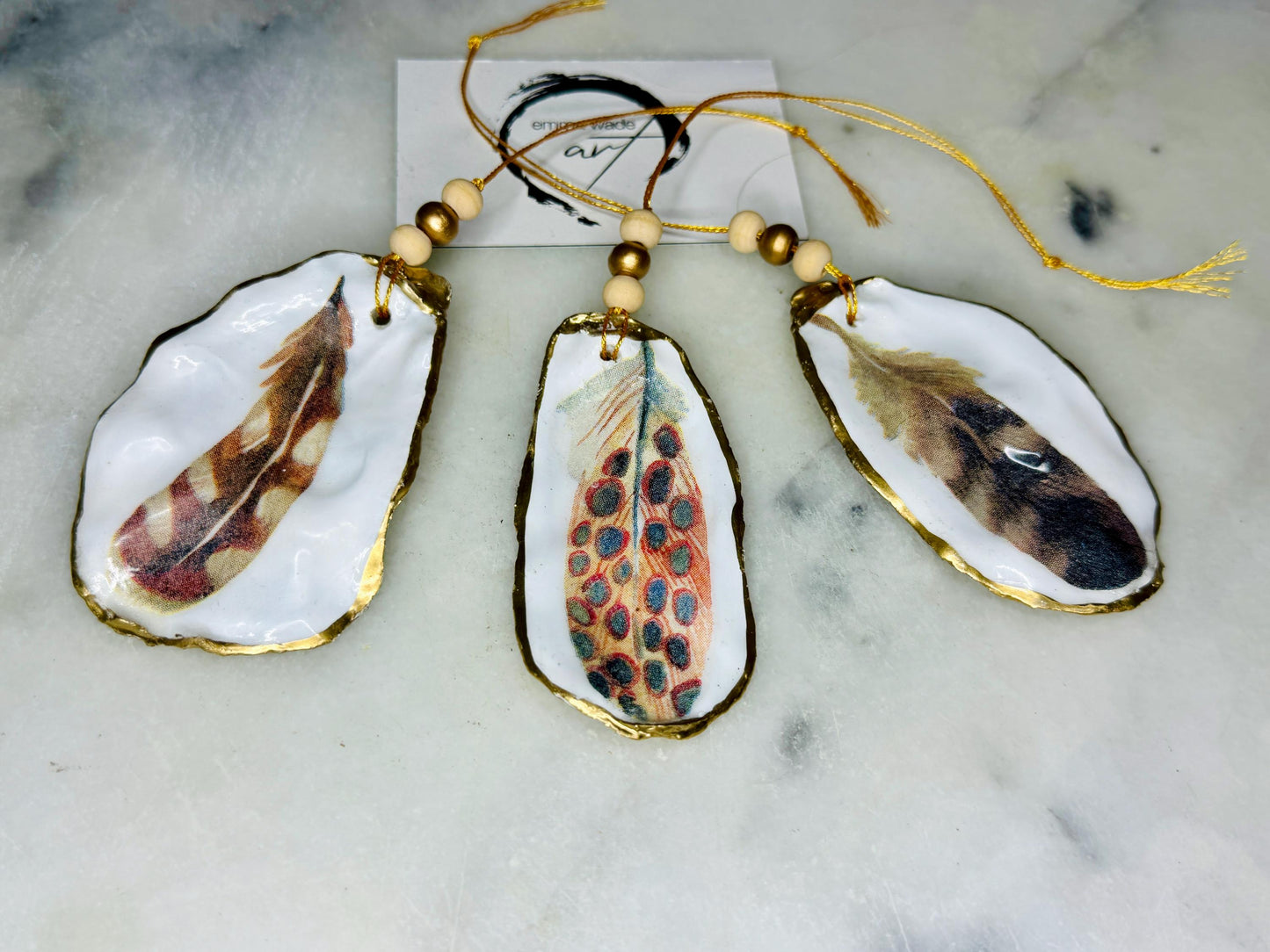 Aquarelle feather oyster shell hanging ornaments, handmade coastal décor, gilded gold leaf shells, resin sealed feather decorations, Christmas tree ornaments, nature-inspired gifts, watercolor feather oyster shells, Dorset handmade shell ornaments, sustainable coastal gifts, oyster shell art, feather design decorations, unique shell ornaments, eco-friendly handmade oyster shell Christmas gifts.