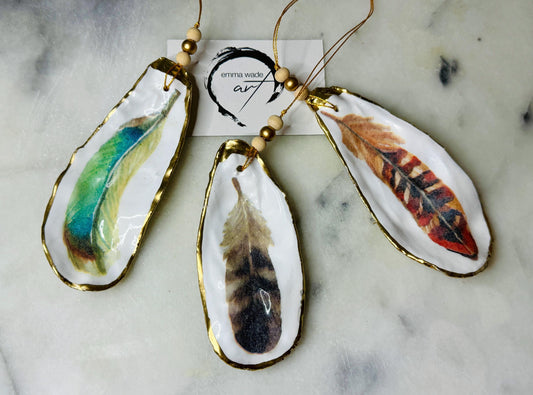 Aquarelle feather oyster shell hanging ornaments, handmade coastal décor, gilded gold leaf shells, resin sealed feather decorations, Christmas tree ornaments, nature-inspired gifts, watercolor feather oyster shells, Dorset handmade shell ornaments, sustainable coastal gifts, oyster shell art, feather design decorations, unique shell ornaments, eco-friendly handmade oyster shell Christmas gifts.