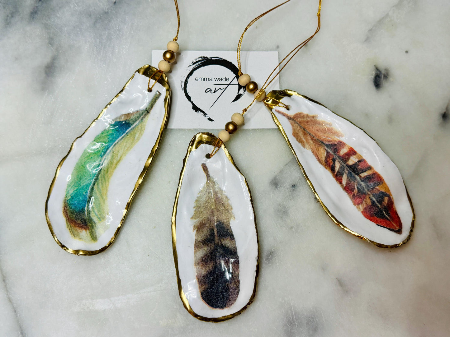 Aquarelle feather oyster shell hanging ornaments, handmade coastal décor, gilded gold leaf shells, resin sealed feather decorations, Christmas tree ornaments, nature-inspired gifts, watercolor feather oyster shells, Dorset handmade shell ornaments, sustainable coastal gifts, oyster shell art, feather design decorations, unique shell ornaments, eco-friendly handmade oyster shell Christmas gifts.