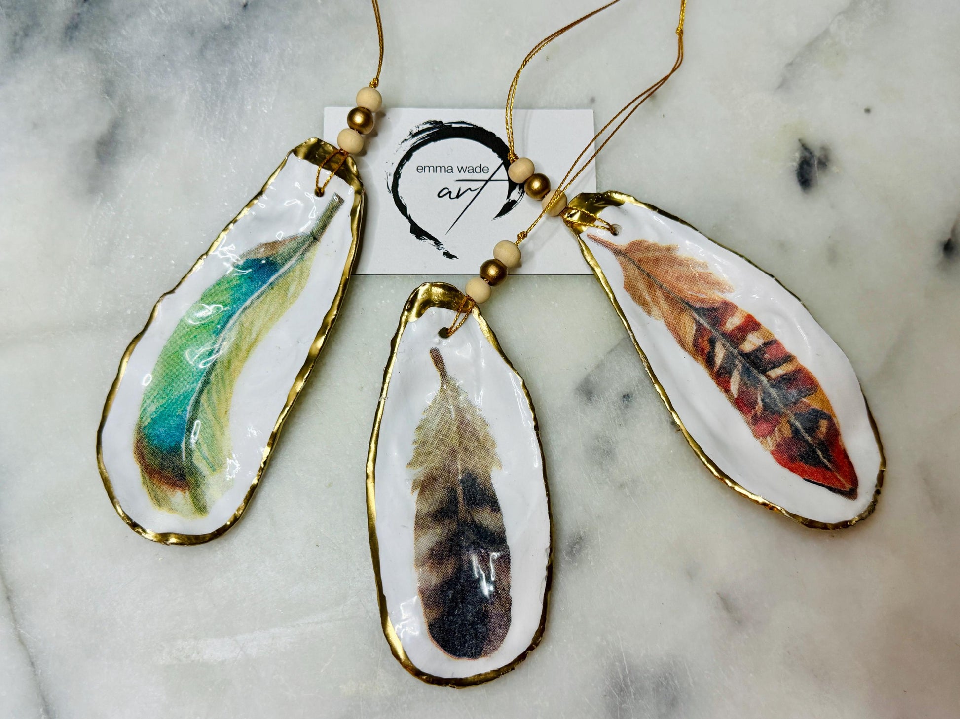 Aquarelle feather oyster shell hanging ornaments, handmade coastal décor, gilded gold leaf shells, resin sealed feather decorations, Christmas tree ornaments, nature-inspired gifts, watercolor feather oyster shells, Dorset handmade shell ornaments, sustainable coastal gifts, oyster shell art, feather design decorations, unique shell ornaments, eco-friendly handmade oyster shell Christmas gifts.