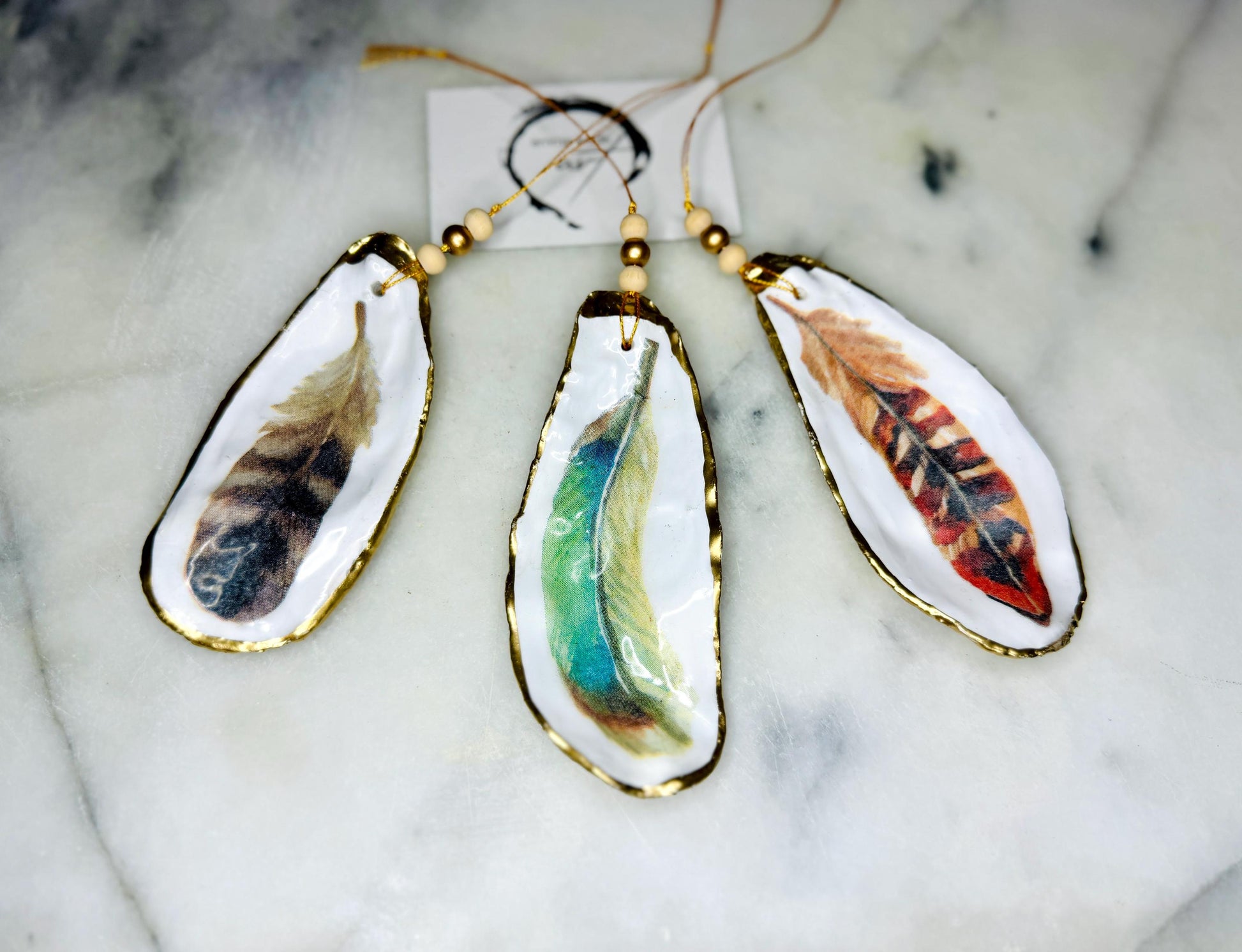 Aquarelle feather oyster shell hanging ornaments, handmade coastal décor, gilded gold leaf shells, resin sealed feather decorations, Christmas tree ornaments, nature-inspired gifts, watercolor feather oyster shells, Dorset handmade shell ornaments, sustainable coastal gifts, oyster shell art, feather design decorations, unique shell ornaments, eco-friendly handmade oyster shell Christmas gifts.