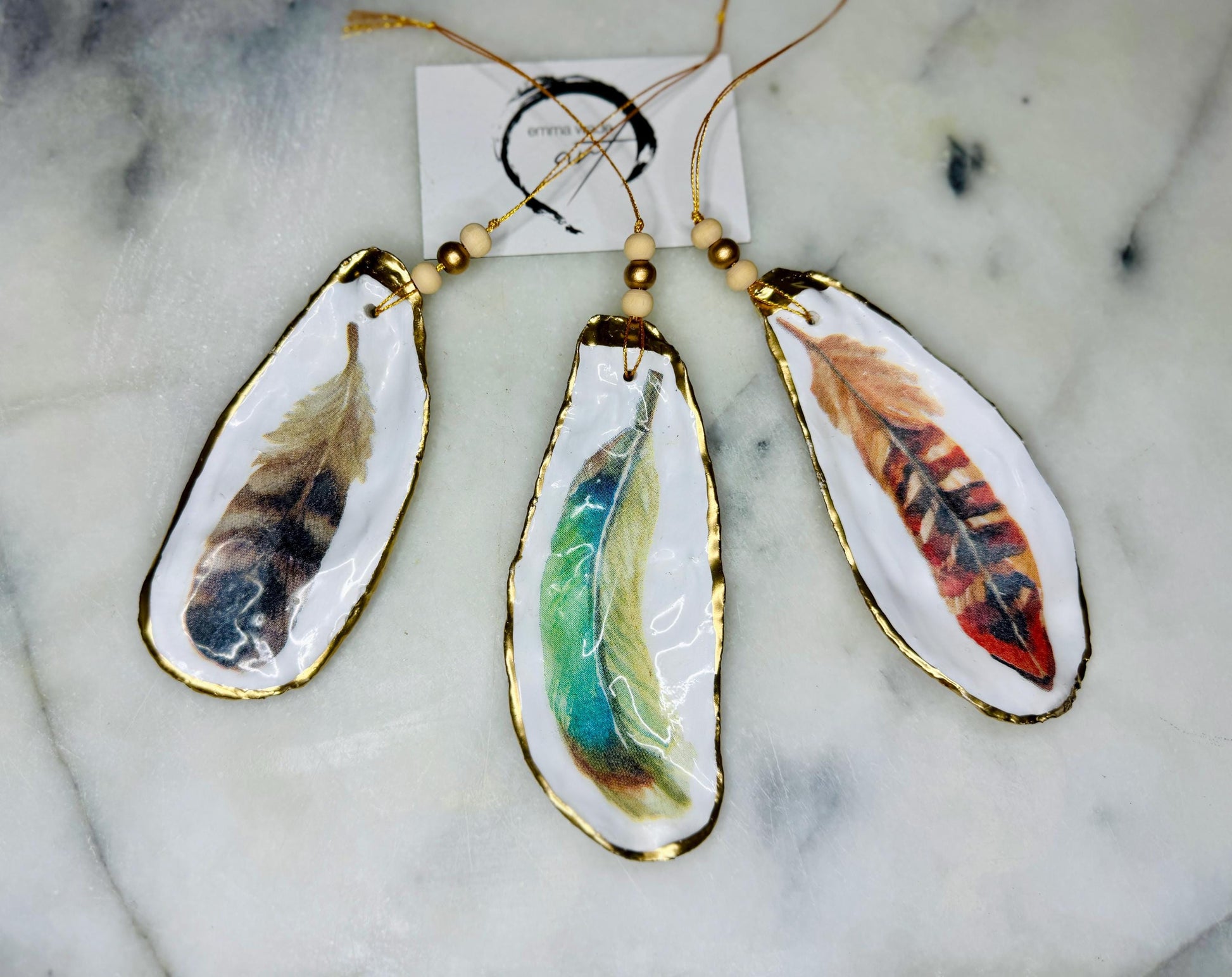Aquarelle feather oyster shell hanging ornaments, handmade coastal décor, gilded gold leaf shells, resin sealed feather decorations, Christmas tree ornaments, nature-inspired gifts, watercolor feather oyster shells, Dorset handmade shell ornaments, sustainable coastal gifts, oyster shell art, feather design decorations, unique shell ornaments, eco-friendly handmade oyster shell Christmas gifts.