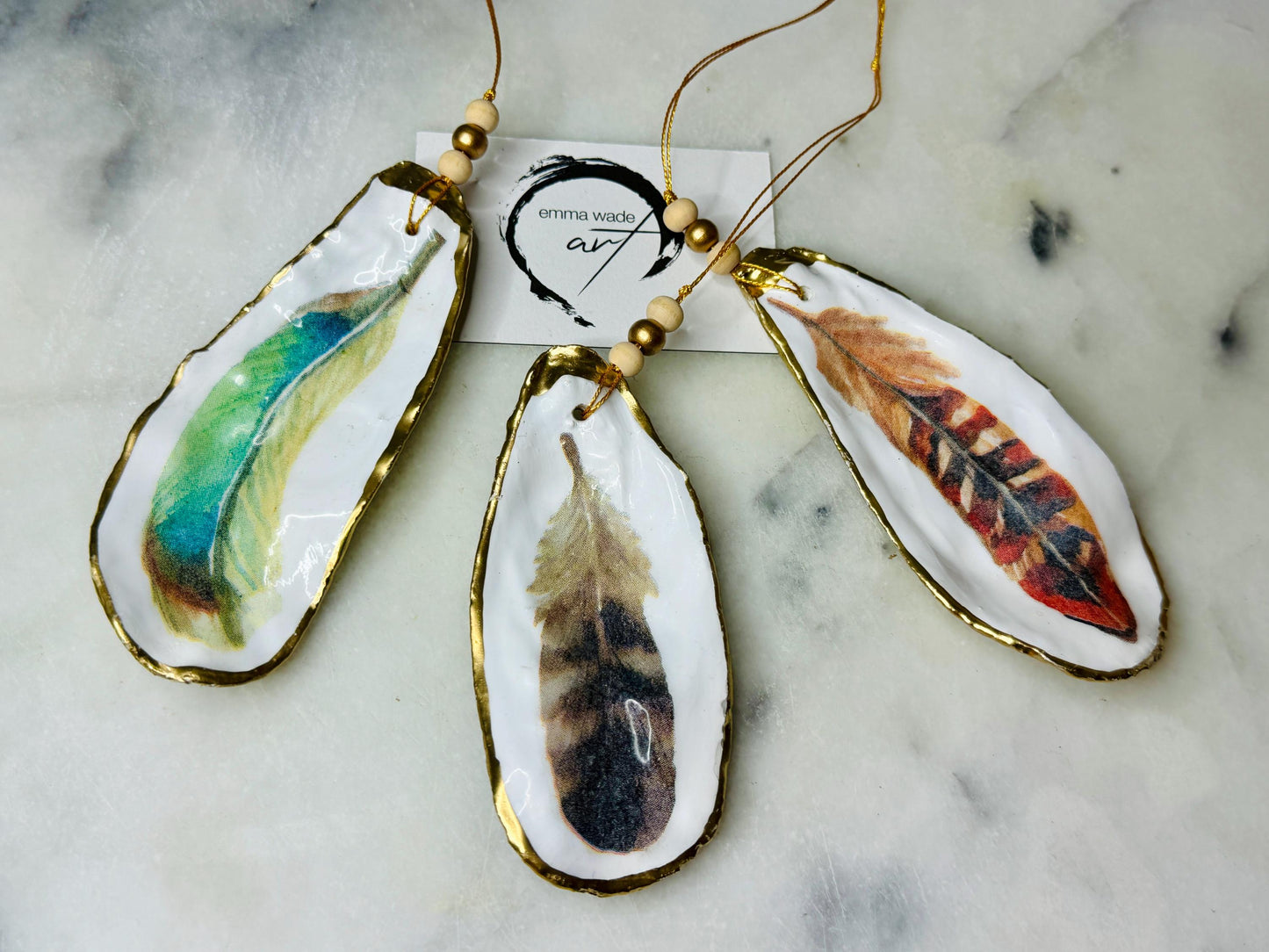 Aquarelle feather oyster shell hanging ornaments, handmade coastal décor, gilded gold leaf shells, resin sealed feather decorations, Christmas tree ornaments, nature-inspired gifts, watercolor feather oyster shells, Dorset handmade shell ornaments, sustainable coastal gifts, oyster shell art, feather design decorations, unique shell ornaments, eco-friendly handmade oyster shell Christmas gifts.