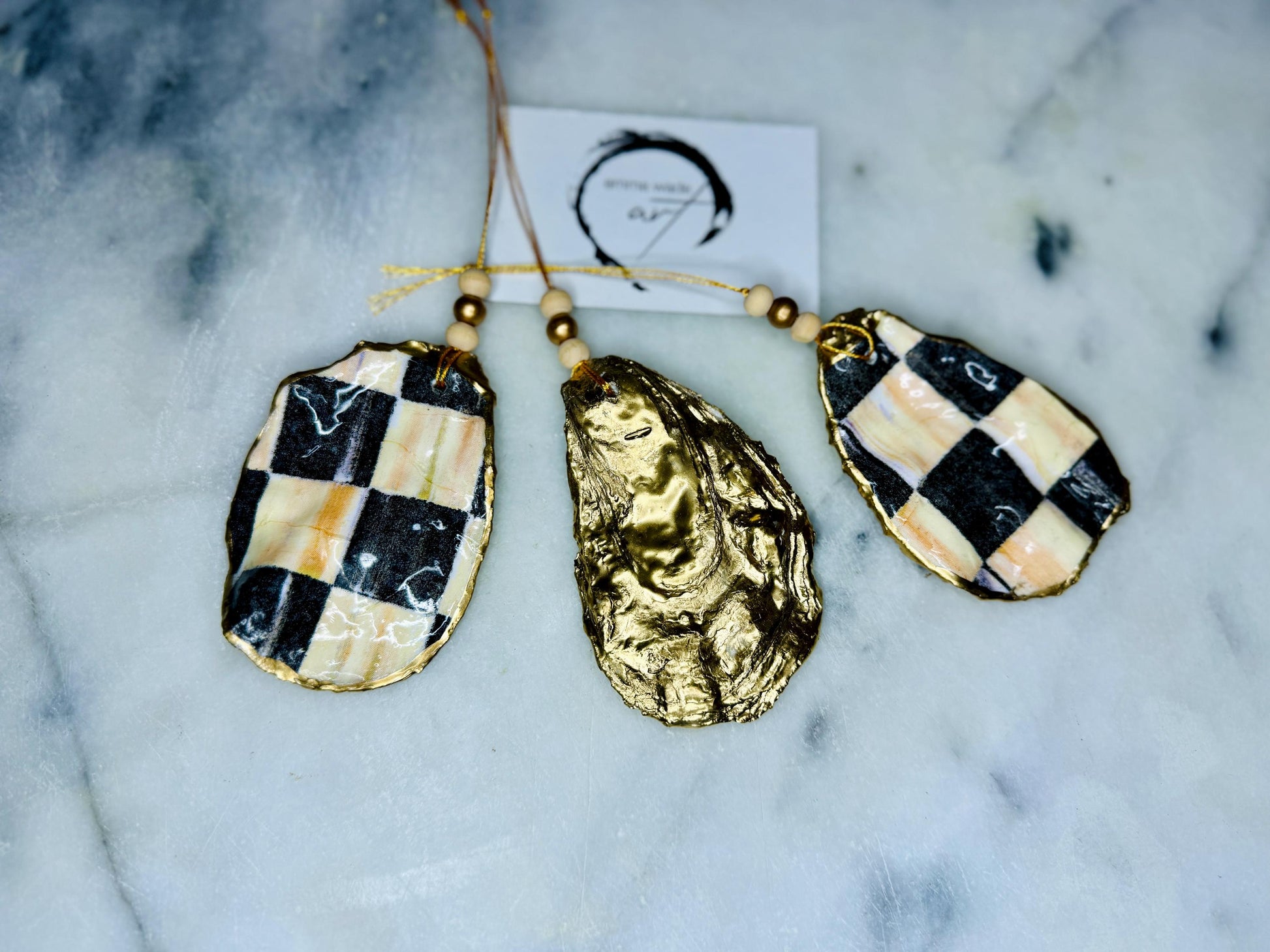 Black and Gold Oyster Shell Hanging Ornament, handmade from Dorset oysters, decoupaged and gilded with liquid gold leaf and sealed with gloss resin. Unique shell Christmas decoration, nautical ornament, chess chequer inspired design. Available individually or as a set of 3. Perfect eco friendly coastal gift, oyster shell bauble, luxury holiday decoration, ocean inspired home décor, handmade oyster art, and nature lover gift.
