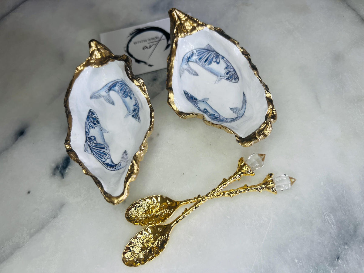 Handmade Dorset oyster shell salt and pepper pinch pots featuring blue paisley fish designs with gold leaf edging and glossy resin finish. Coastal oyster shell cruet set with natural pearlescent interiors and optional gold spoons, styled as elegant nautical table décor and condiment dishes.