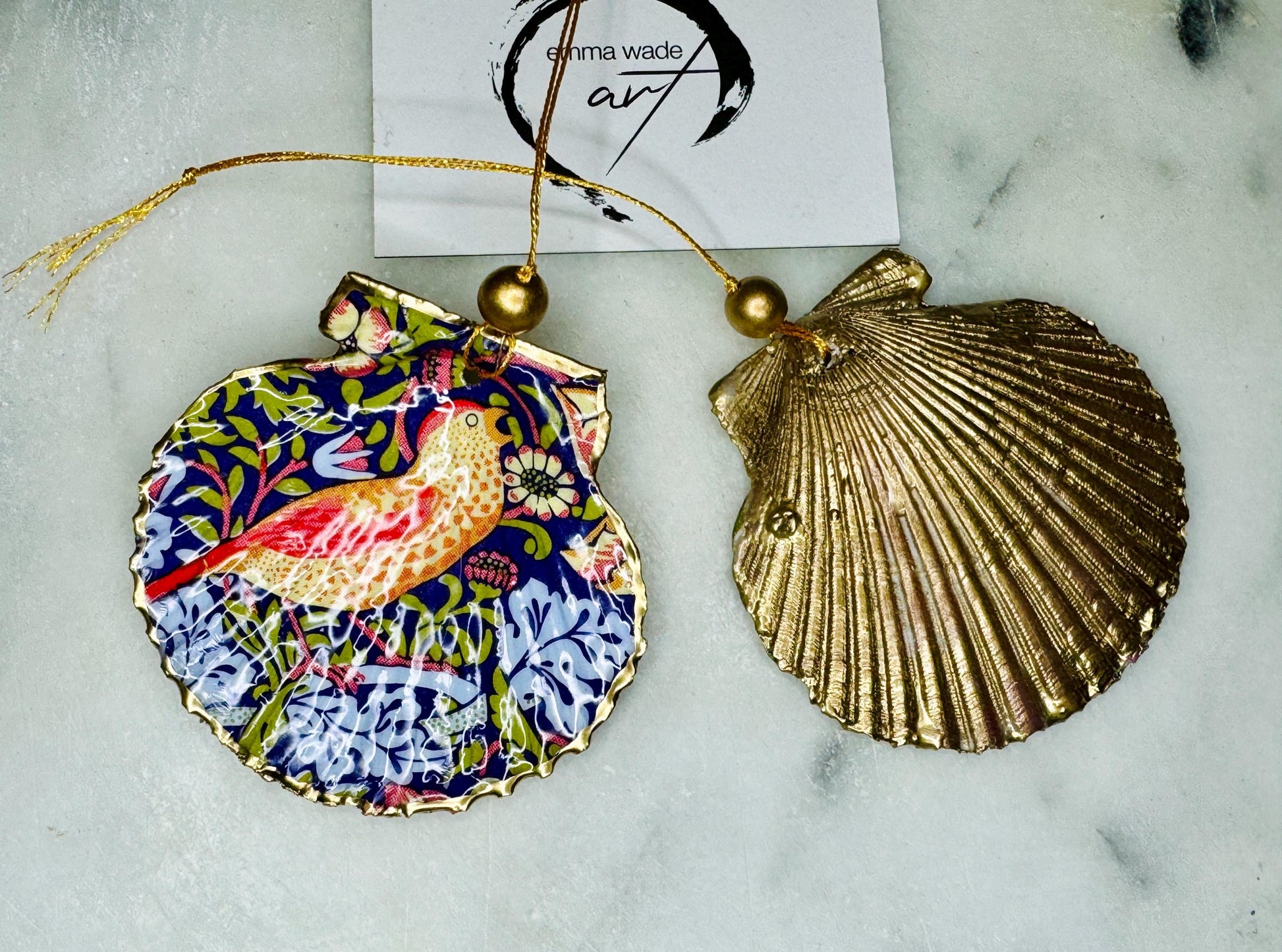 Handmade William Morris Strawberry Thief scallop shell hanging ornaments in four colourways with birds, floral patterns and gold leaf edging. Coastal shell ornaments finished in glossy resin with gold hanging cords for Christmas trees or year-round home decor. UK Heritage Gift