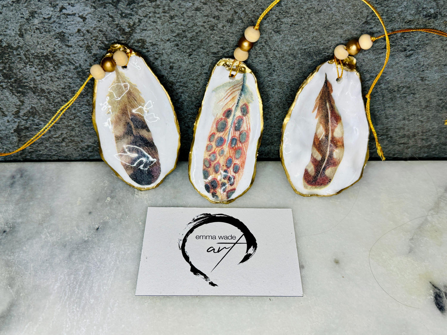 Aquarelle feather oyster shell hanging ornaments, handmade coastal décor, gilded gold leaf shells, resin sealed feather decorations, Christmas tree ornaments, nature-inspired gifts, watercolor feather oyster shells, Dorset handmade shell ornaments, sustainable coastal gifts, oyster shell art, feather design decorations, unique shell ornaments, eco-friendly handmade oyster shell Christmas gifts.