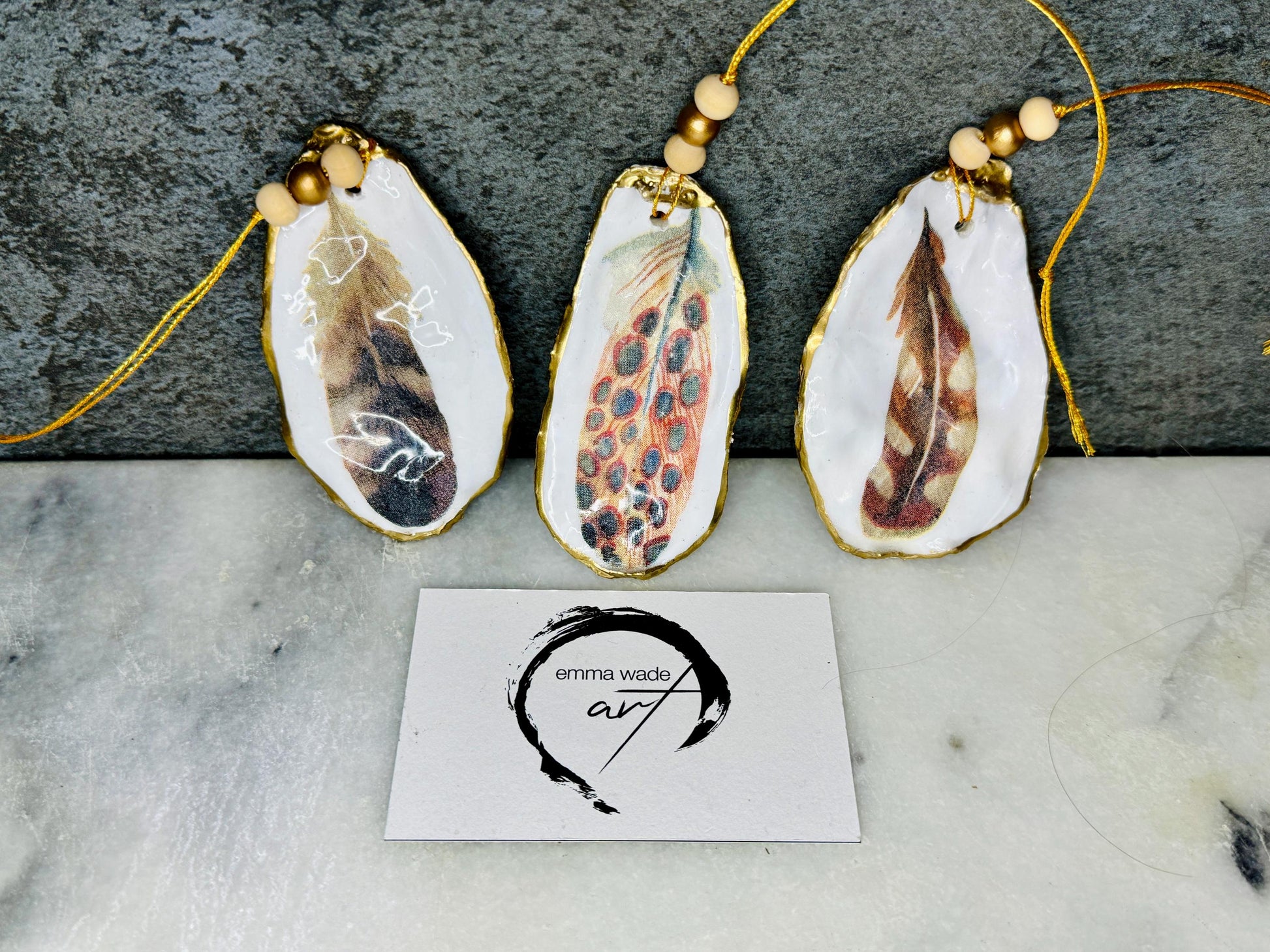 Aquarelle feather oyster shell hanging ornaments, handmade coastal décor, gilded gold leaf shells, resin sealed feather decorations, Christmas tree ornaments, nature-inspired gifts, watercolor feather oyster shells, Dorset handmade shell ornaments, sustainable coastal gifts, oyster shell art, feather design decorations, unique shell ornaments, eco-friendly handmade oyster shell Christmas gifts.