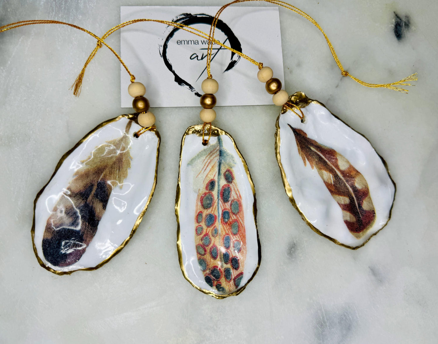 Aquarelle feather oyster shell hanging ornaments, handmade coastal décor, gilded gold leaf shells, resin sealed feather decorations, Christmas tree ornaments, nature-inspired gifts, watercolor feather oyster shells, Dorset handmade shell ornaments, sustainable coastal gifts, oyster shell art, feather design decorations, unique shell ornaments, eco-friendly handmade oyster shell Christmas gifts.