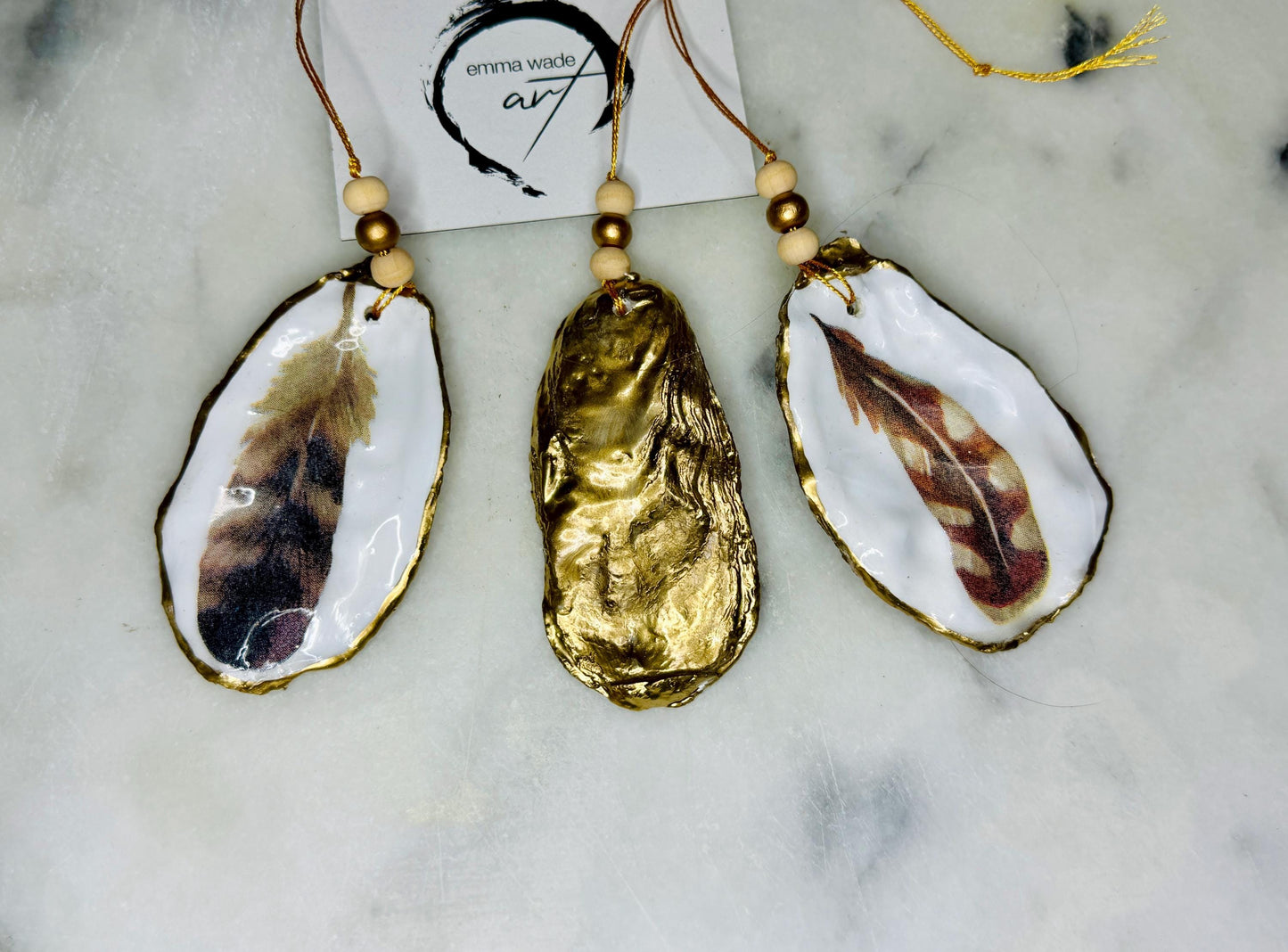 Aquarelle feather oyster shell hanging ornaments, handmade coastal décor, gilded gold leaf shells, resin sealed feather decorations, Christmas tree ornaments, nature-inspired gifts, watercolor feather oyster shells, Dorset handmade shell ornaments, sustainable coastal gifts, oyster shell art, feather design decorations, unique shell ornaments, eco-friendly handmade oyster shell Christmas gifts.