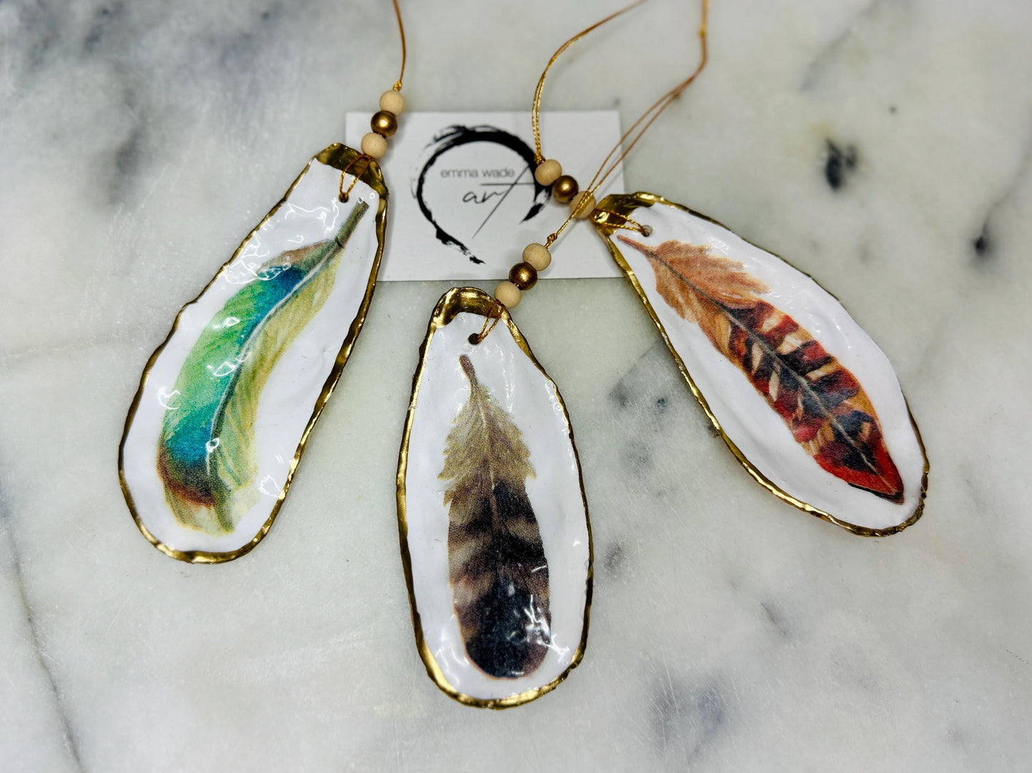 Aquarelle feather oyster shell hanging ornaments, handmade coastal décor, gilded gold leaf shells, resin sealed feather decorations, Christmas tree ornaments, nature-inspired gifts, watercolor feather oyster shells, Dorset handmade shell ornaments, sustainable coastal gifts, oyster shell art, feather design decorations, unique shell ornaments, eco-friendly handmade oyster shell Christmas gifts.
