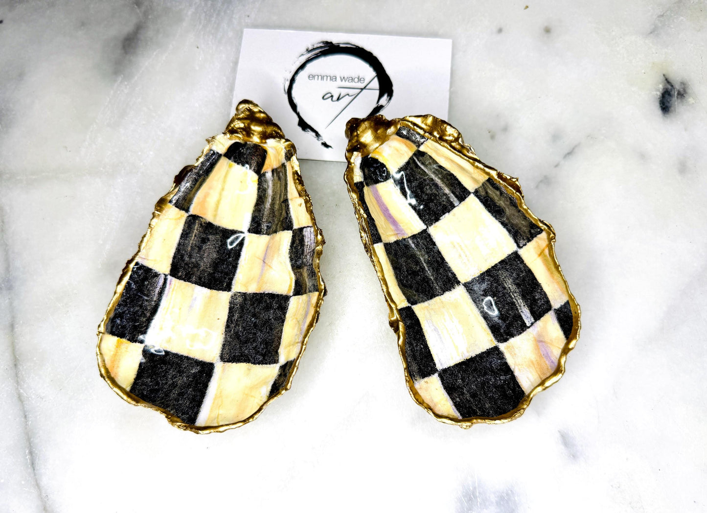 Black and gold chequered oyster shell dish with liquid gold leaf edging and glossy resin finish. A unique oyster ring dish, oyster ring tray, or shell jewellery organiser for rings, earrings, and cufflinks. This handmade trinket tray doubles as a jewellery dish or decorative coastal accent. Crafted from Dorset shells, each piece is one of a kind. A thoughtful handmade gift for weddings, anniversaries, birthdays, Christmas, bridesmaids, or new home celebrations.