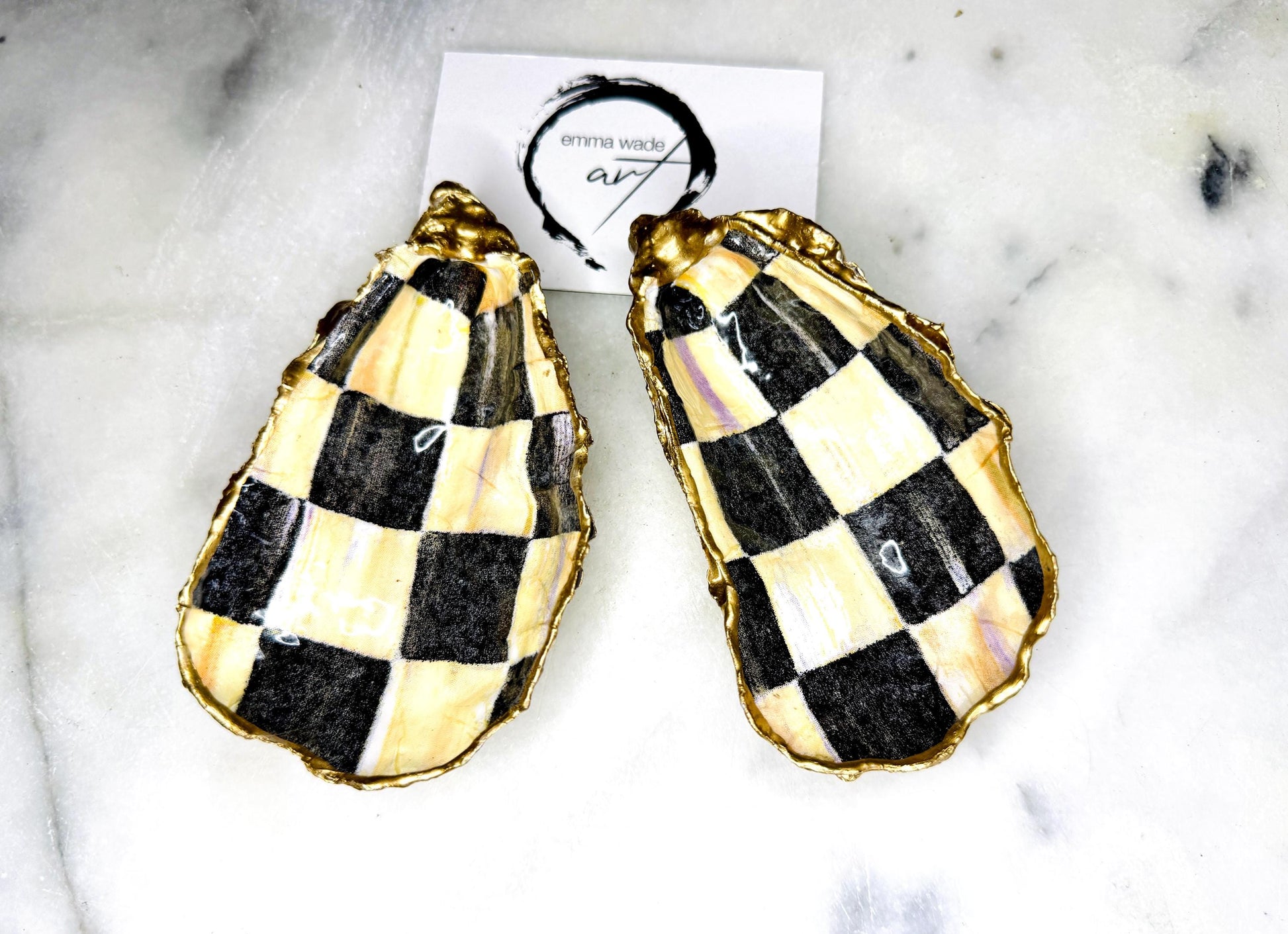 Black and gold chequered oyster shell dish with liquid gold leaf edging and glossy resin finish. A unique oyster ring dish, oyster ring tray, or shell jewellery organiser for rings, earrings, and cufflinks. This handmade trinket tray doubles as a jewellery dish or decorative coastal accent. Crafted from Dorset shells, each piece is one of a kind. A thoughtful handmade gift for weddings, anniversaries, birthdays, Christmas, bridesmaids, or new home celebrations.