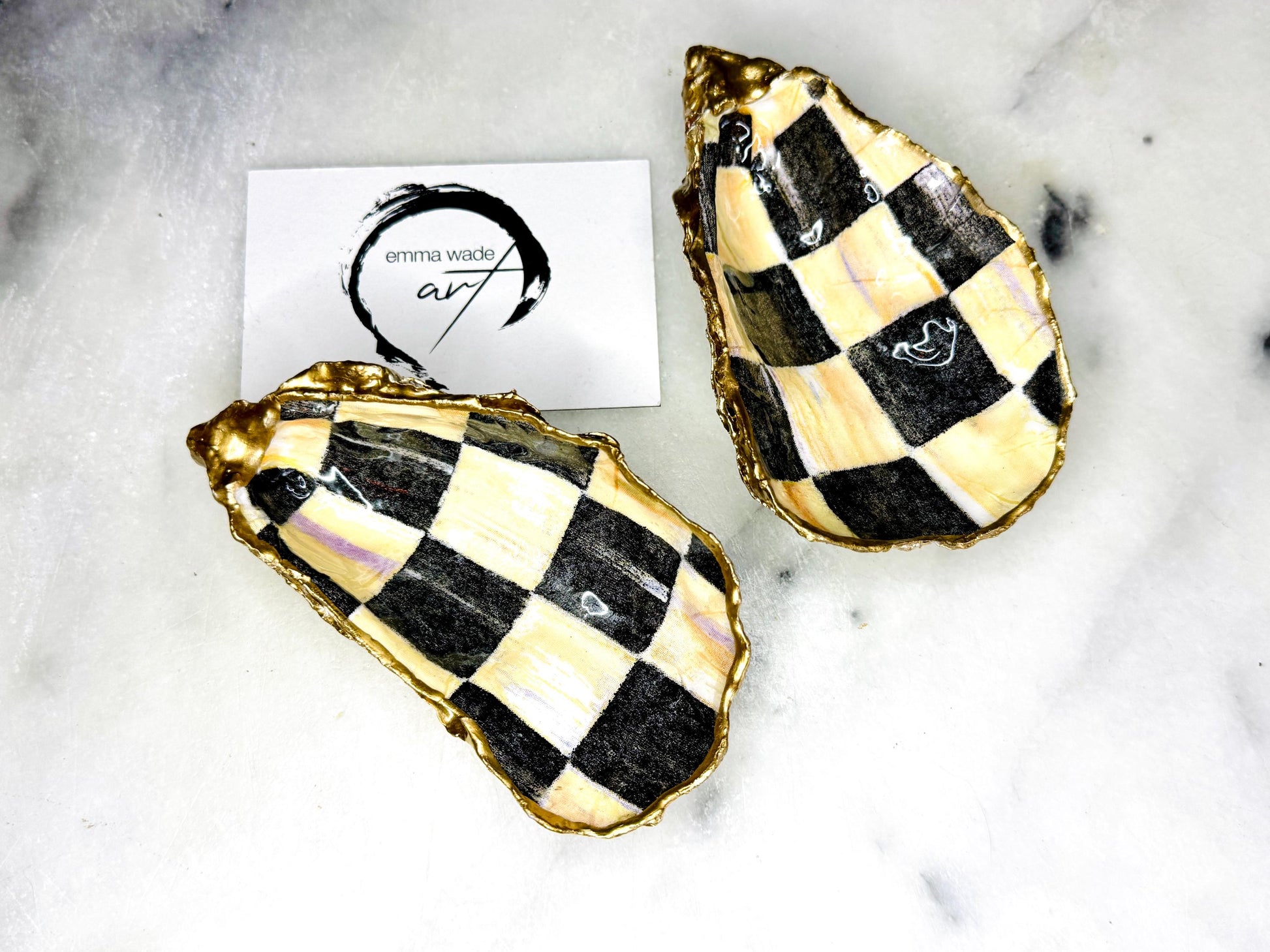Handmade black, pearl and gold chequered oyster shell salt and pepper pinch pots, shown as a matching pair with small gold spoons on a light background. Natural Dorset shells decorated with a graphic pattern, gilded with gold leaf and sealed with a glossy, food-safe resin. Elegant coastal table decor and a unique gift for weddings, anniversaries or stylish dining tables, each piece one of a kind.