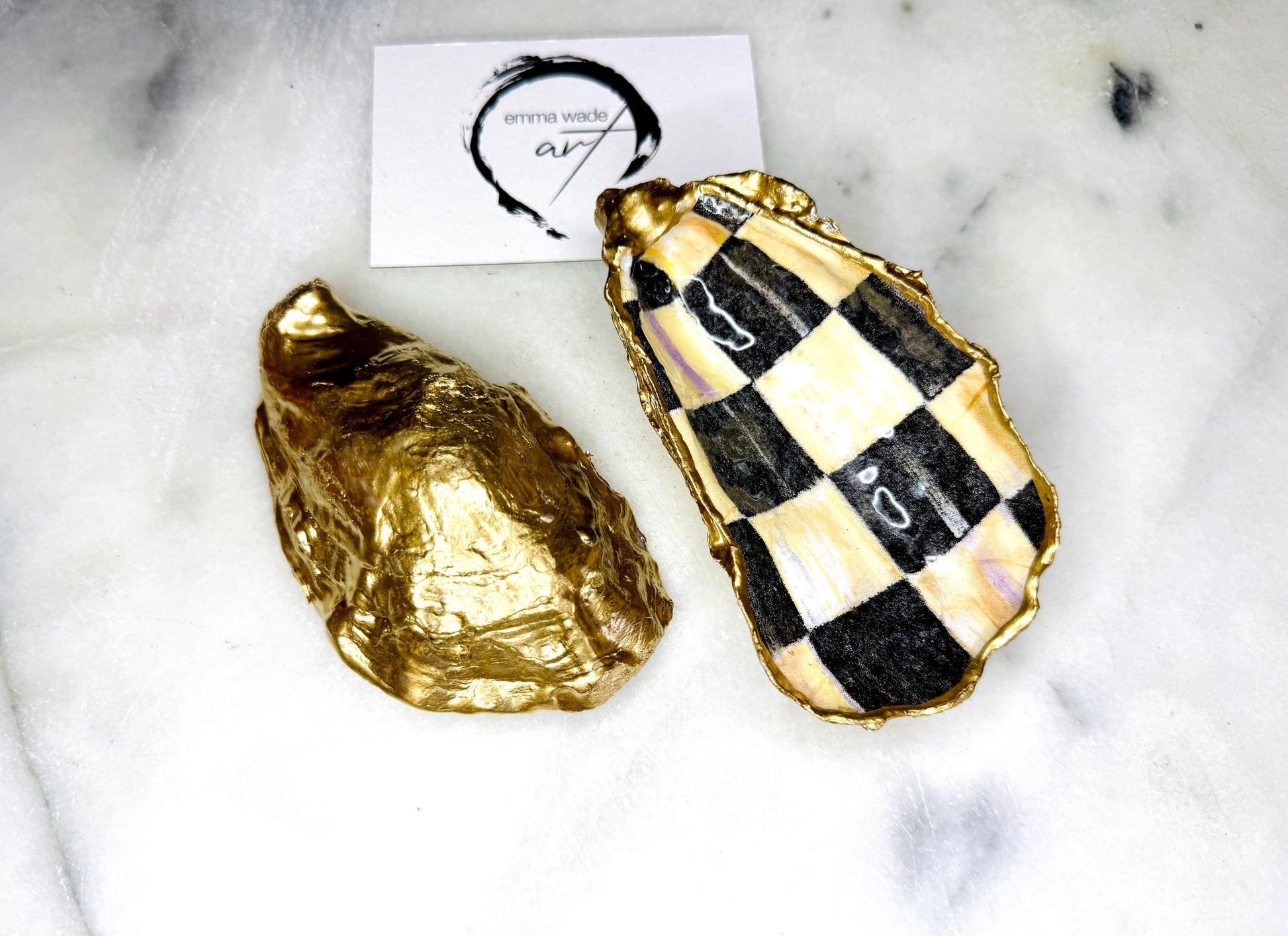 Handmade black, pearl and gold chequered oyster shell salt and pepper pinch pots, shown as a matching pair with small gold spoons on a light background. Natural Dorset shells decorated with a graphic pattern, gilded with gold leaf and sealed with a glossy, food-safe resin. Elegant coastal table decor and a unique gift for weddings, anniversaries or stylish dining tables, each piece one of a kind.