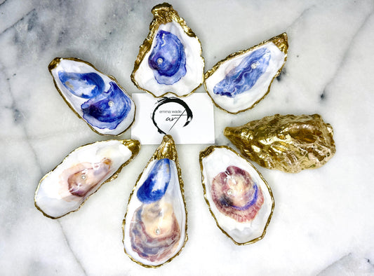 Handmade Dorset oyster shell trinket dish featuring a blue and beige watercolour oyster illustration with Swarovski pearl detail, finished with hand-applied gold leaf edging and glossy resin. Coastal-inspired jewellery dish and ring holder available in multiple sizes including XL oyster shells. Elegant handmade coastal décor gift ideal for weddings, birthdays, anniversaries, and luxury beach house interiors.