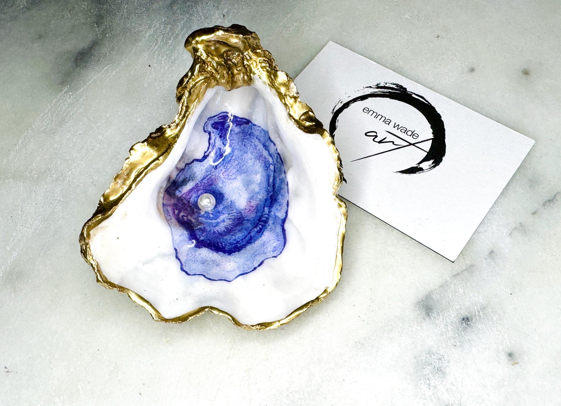 Handmade Dorset oyster shell trinket dish featuring a blue and beige watercolour oyster illustration with Swarovski pearl detail, finished with hand-applied gold leaf edging and glossy resin. Coastal-inspired jewellery dish and ring holder available in multiple sizes including XL oyster shells. Elegant handmade coastal décor gift ideal for weddings, birthdays, anniversaries, and luxury beach house interiors.