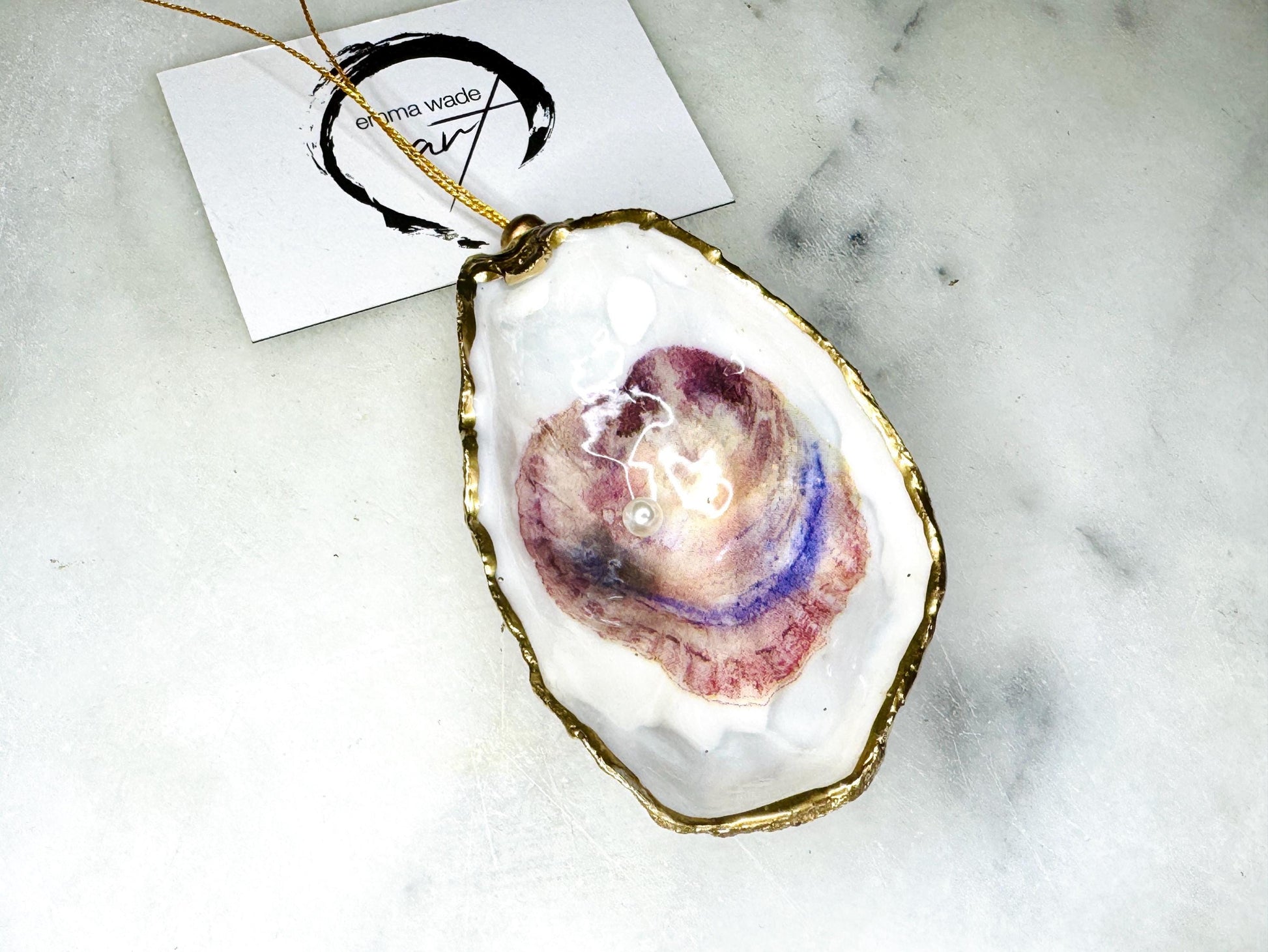Handcrafted Dorset oyster shell hanging ornament decorated with a Swarovski pearl. Each natural oyster shell is finished with liquid gold leaf on the rim and back, sealed with crystal-clear glossy resin, and strung with gold cord and bead. Unique coastal Christmas decoration or tree bauble that can also be displayed year-round. A beautiful handmade oyster shell gift, ideal for weddings, anniversaries, Christmas stockings, bridesmaid keepsakes, or coastal-inspired home décor.