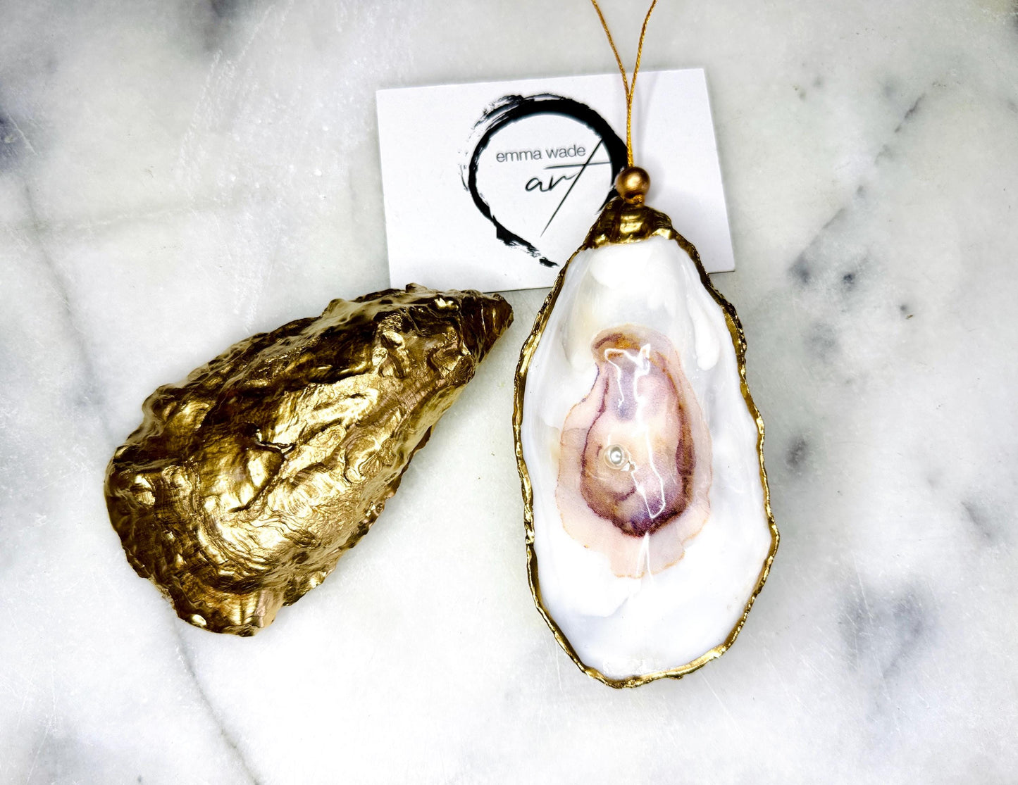 Handcrafted Dorset oyster shell hanging ornament decorated with a Swarovski pearl. Each natural oyster shell is finished with liquid gold leaf on the rim and back, sealed with crystal-clear glossy resin, and strung with gold cord and bead. Unique coastal Christmas decoration or tree bauble that can also be displayed year-round. A beautiful handmade oyster shell gift, ideal for weddings, anniversaries, Christmas stockings, bridesmaid keepsakes, or coastal-inspired home décor.