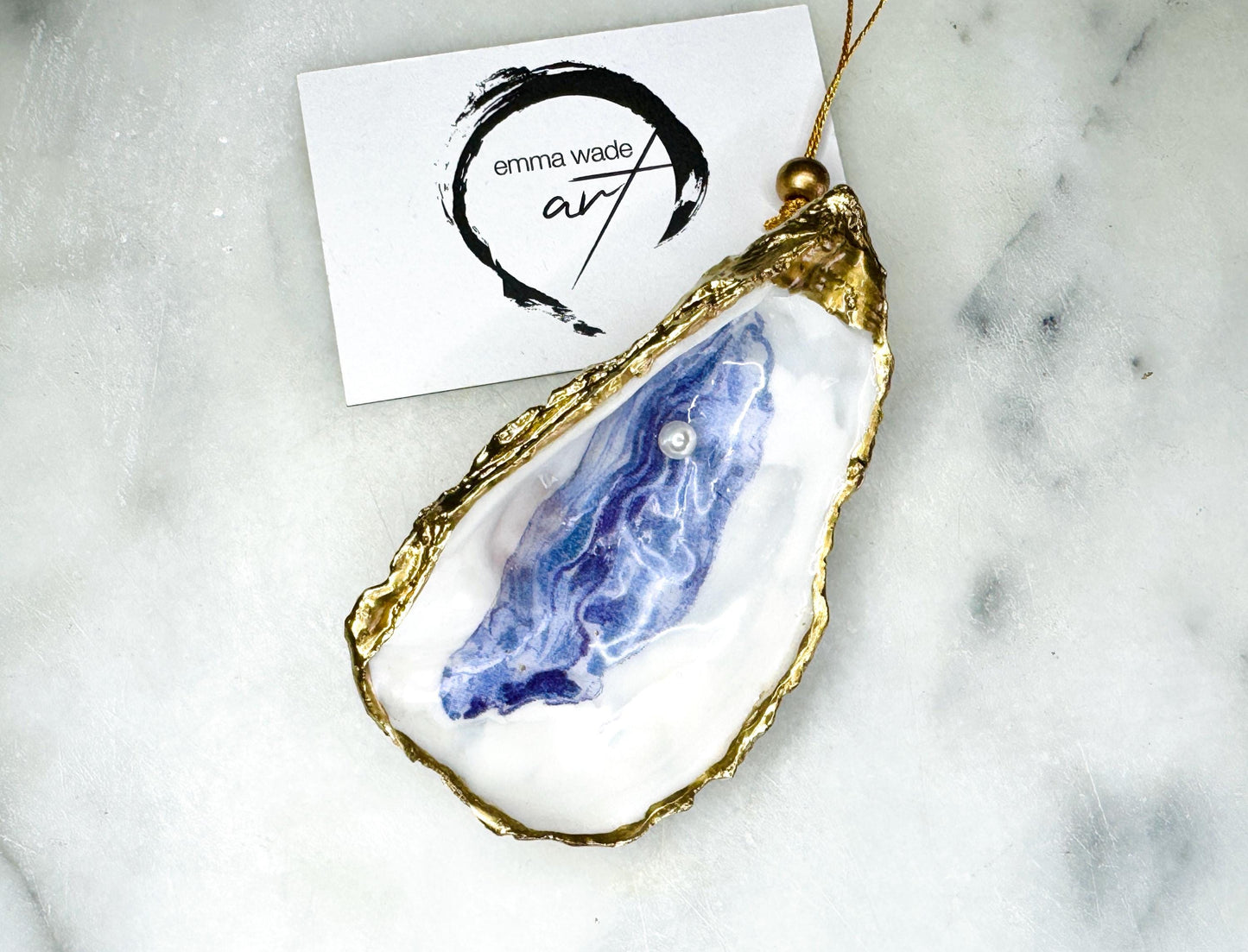 Handcrafted Dorset oyster shell hanging ornament decorated with a Swarovski pearl. Each natural oyster shell is finished with liquid gold leaf on the rim and back, sealed with crystal-clear glossy resin, and strung with gold cord and bead. Unique coastal Christmas decoration or tree bauble that can also be displayed year-round. A beautiful handmade oyster shell gift, ideal for weddings, anniversaries, Christmas stockings, bridesmaid keepsakes, or coastal-inspired home décor.