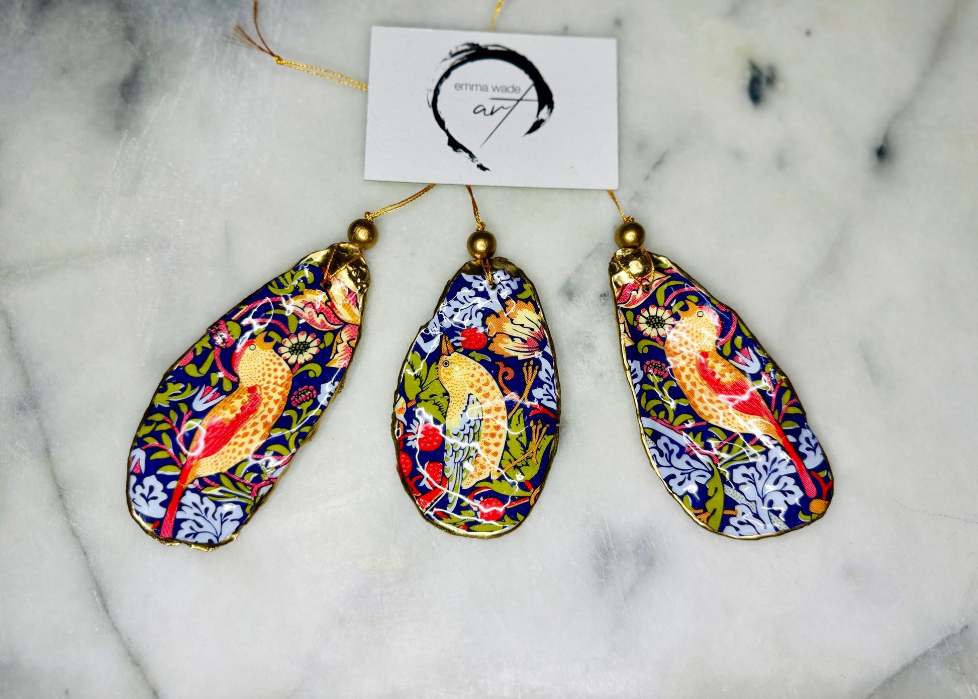Handmade flat oyster shell ornaments decorated with William Morris Red Strawberry Thief design. Each Dorset shell has a natural pearl finish, gilded with liquid gold leaf on the rim and back, and sealed with glossy resin for durability and shine. Pre-drilled with gold string and bead for easy hanging. Available individually, as a set of 3, or set of 6. Unique coastal-inspired decorations, perfect as Christmas tree ornaments, wedding favours, bridesmaid gifts, or handmade William Morris presents.