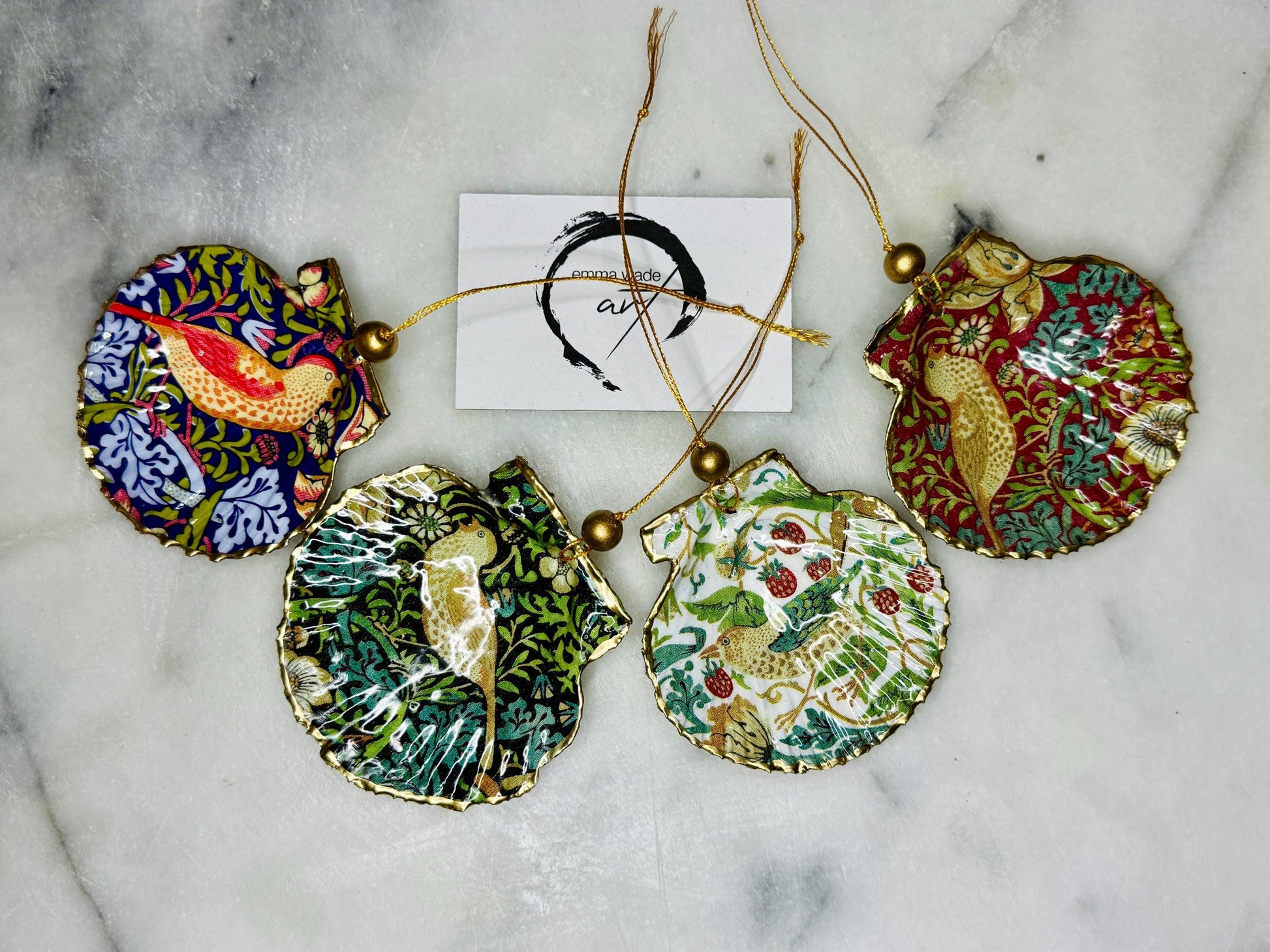Handmade William Morris Strawberry Thief scallop shell hanging ornaments in four colourways with birds, floral patterns and gold leaf edging. Coastal shell ornaments finished in glossy resin with gold hanging cords for Christmas trees or year-round home decor. UK Heritage Gift