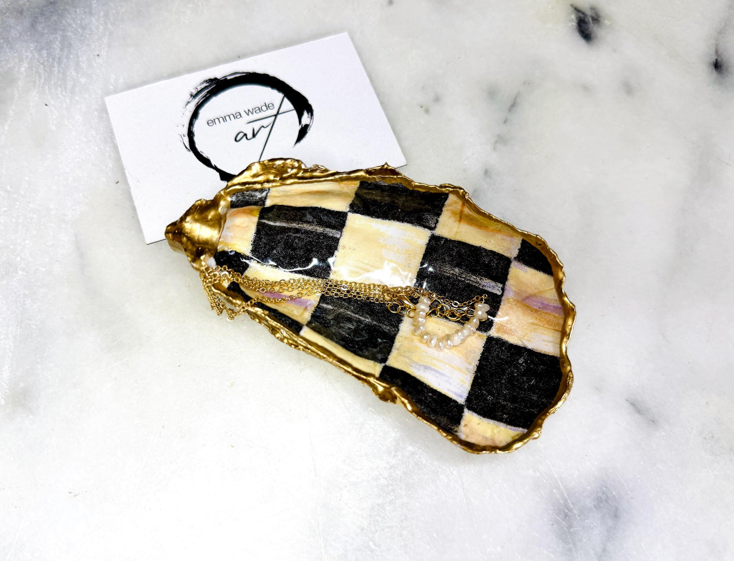 Black and gold chequered oyster shell dish with liquid gold leaf edging and glossy resin finish. A unique oyster ring dish, oyster ring tray, or shell jewellery organiser for rings, earrings, and cufflinks. This handmade trinket tray doubles as a jewellery dish or decorative coastal accent. Crafted from Dorset shells, each piece is one of a kind. A thoughtful handmade gift for weddings, anniversaries, birthdays, Christmas, bridesmaids, or new home celebrations.